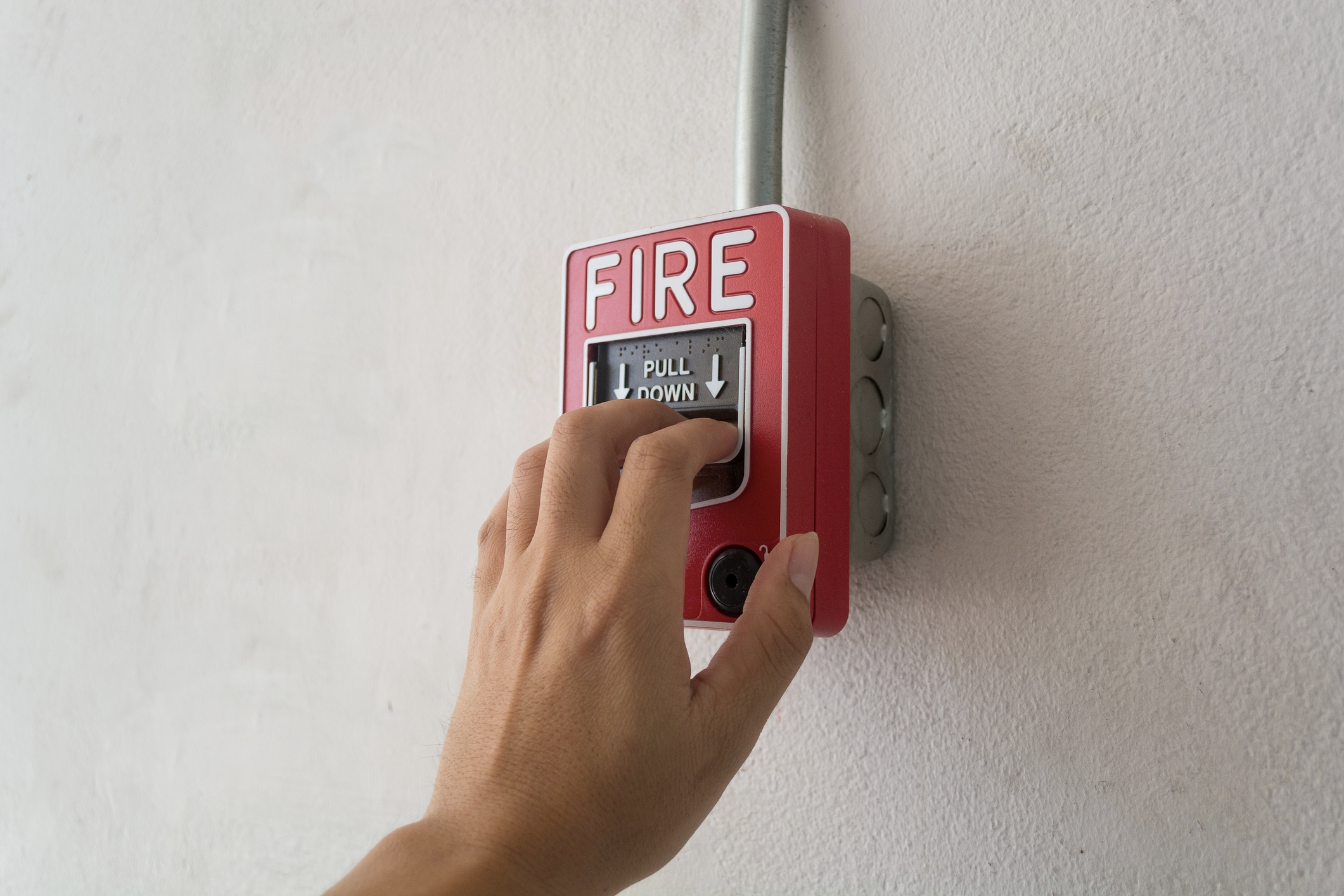 A hand is pulling down a fire alarm lever on a wall-mounted fixture