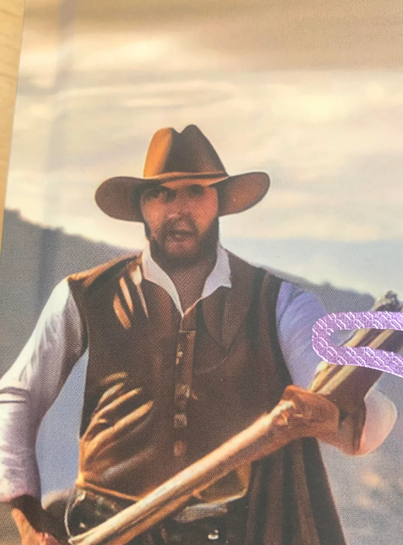 Person in cowboy attire holding a rifle with a holster over their shoulder, set in an outdoor landscape