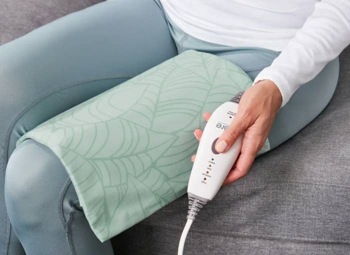 Person sitting connected  a sofa  uses a heating pad connected  their knee, holding a power  instrumentality  for somesthesia  settings