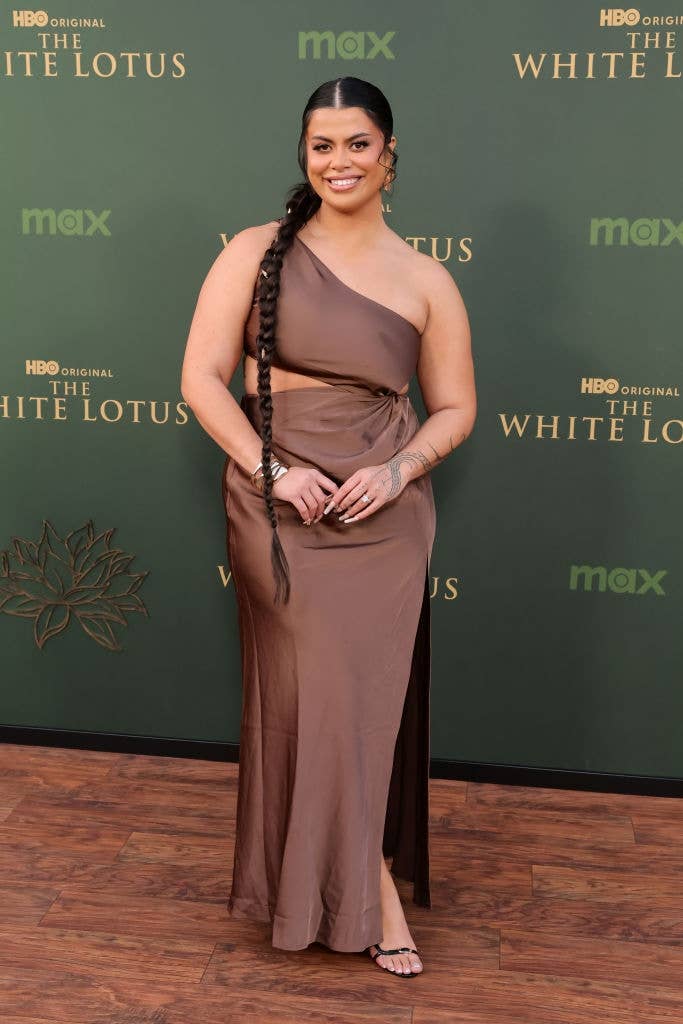Person successful a one-shoulder, flowing gown with a agelong braid, posing astatine "The White Lotus" lawsuit backdrop