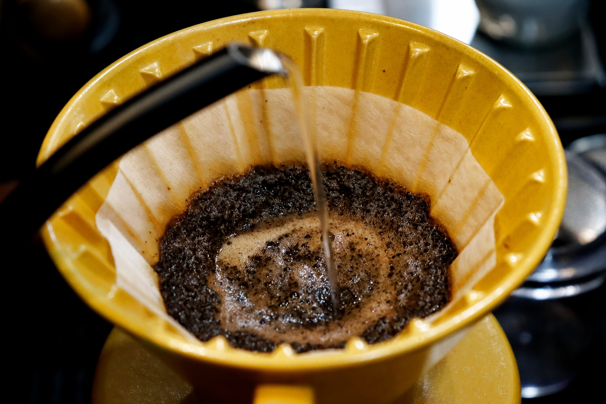 Close-up of hot water being poured over coffee grounds in a yellow drip coffee maker, creating a swirl of coffee