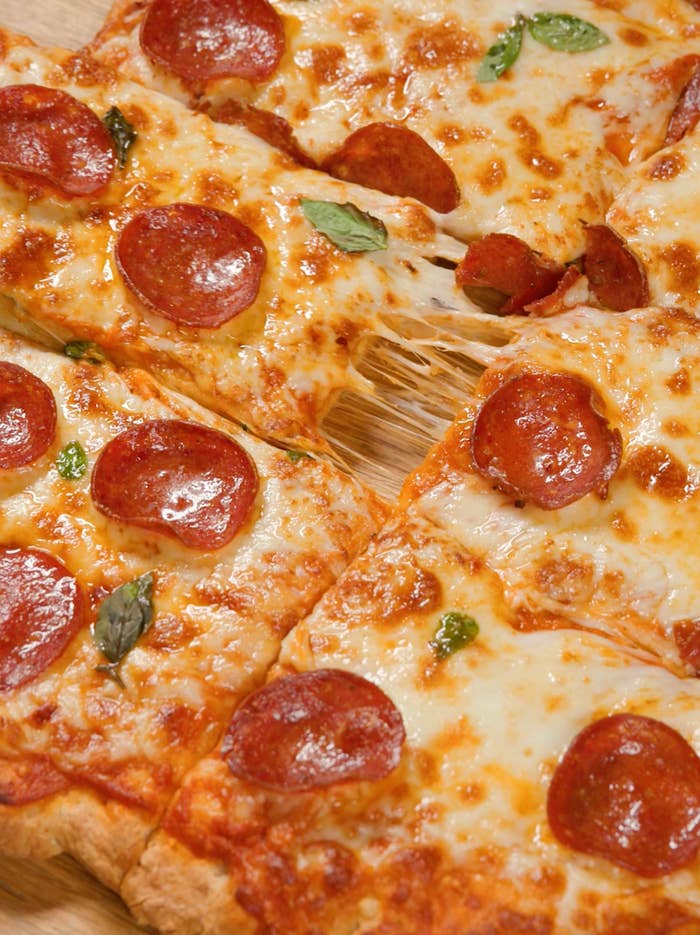 Pizza with pepperoni and melted cheese, garnished with caller  basil, sliced into 8  pieces connected  a woody  board