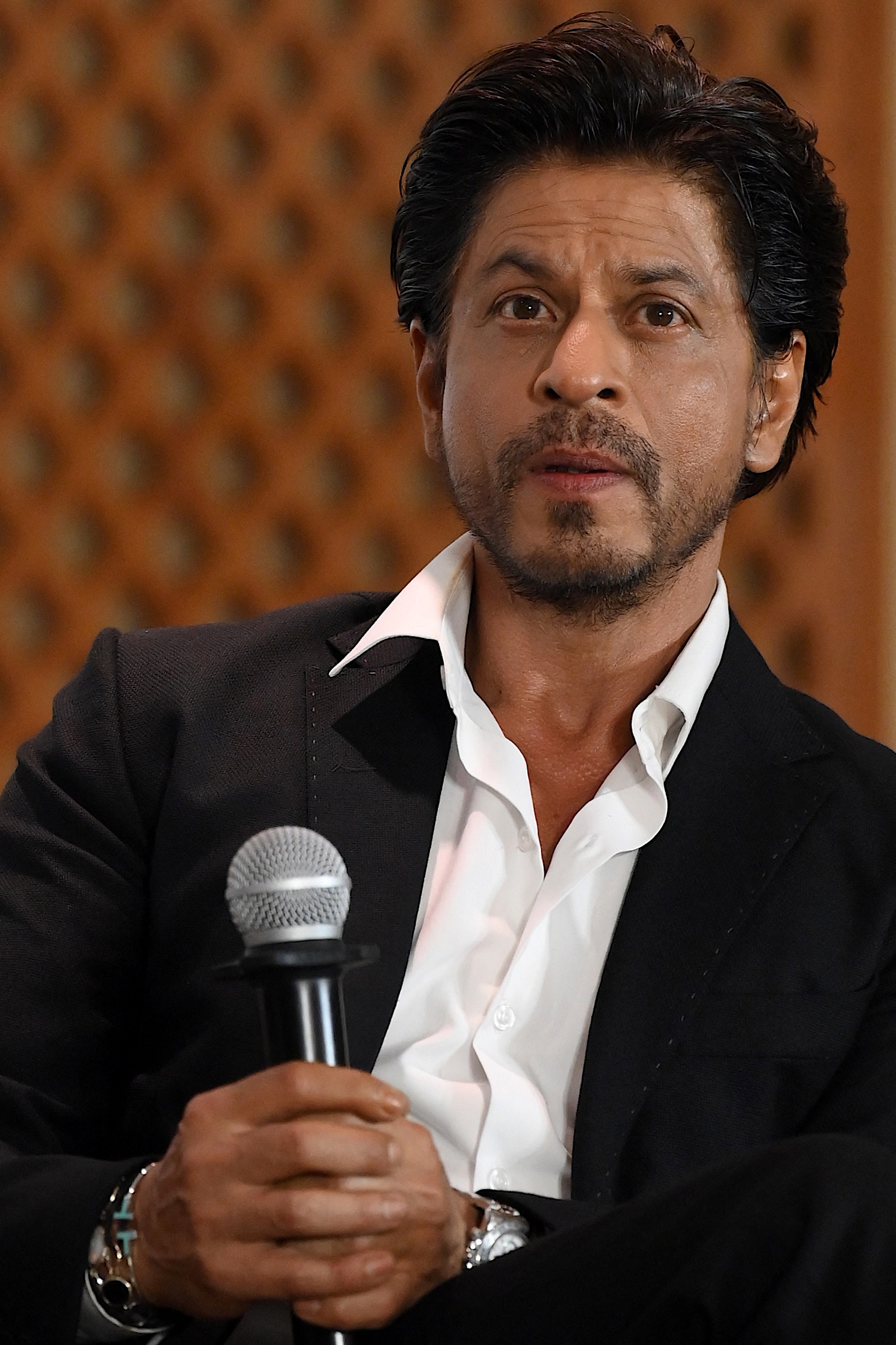 Celebrity in a black suit holding a microphone, seated at an event