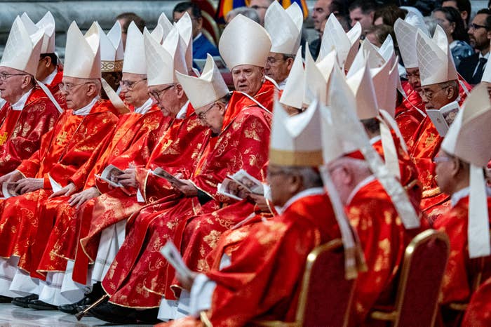 A group of clergy in ornate robes and mitres seated in a church setting, holding papers