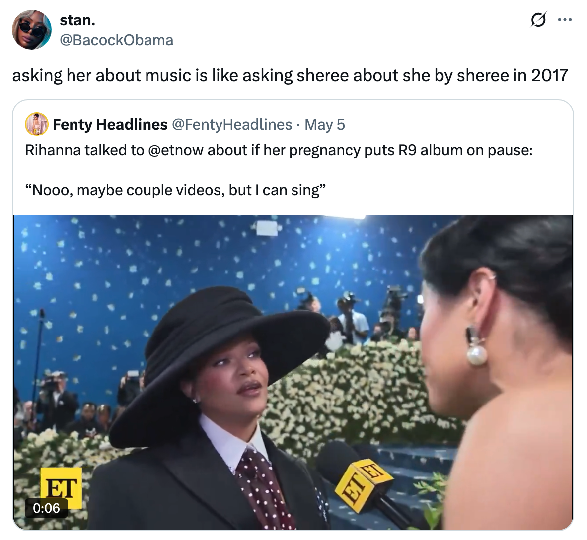 Rihanna, wearing a hat and polka dot tie, being interviewed on a red carpet at an event. There's a floral backdrop behind her