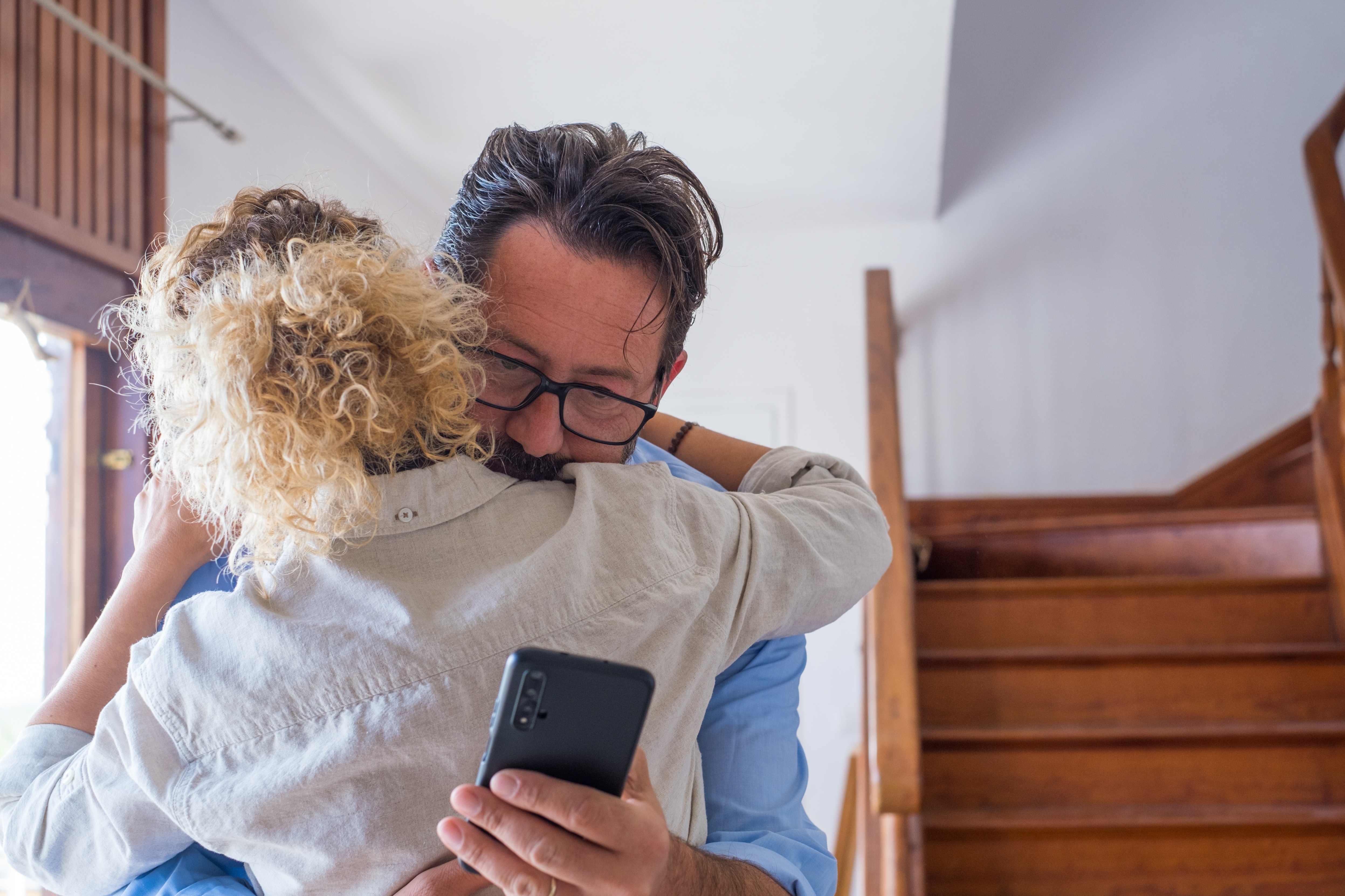 A person hugs another while holding a phone behind their back, suggesting hidden communication or secrecy in a relationship