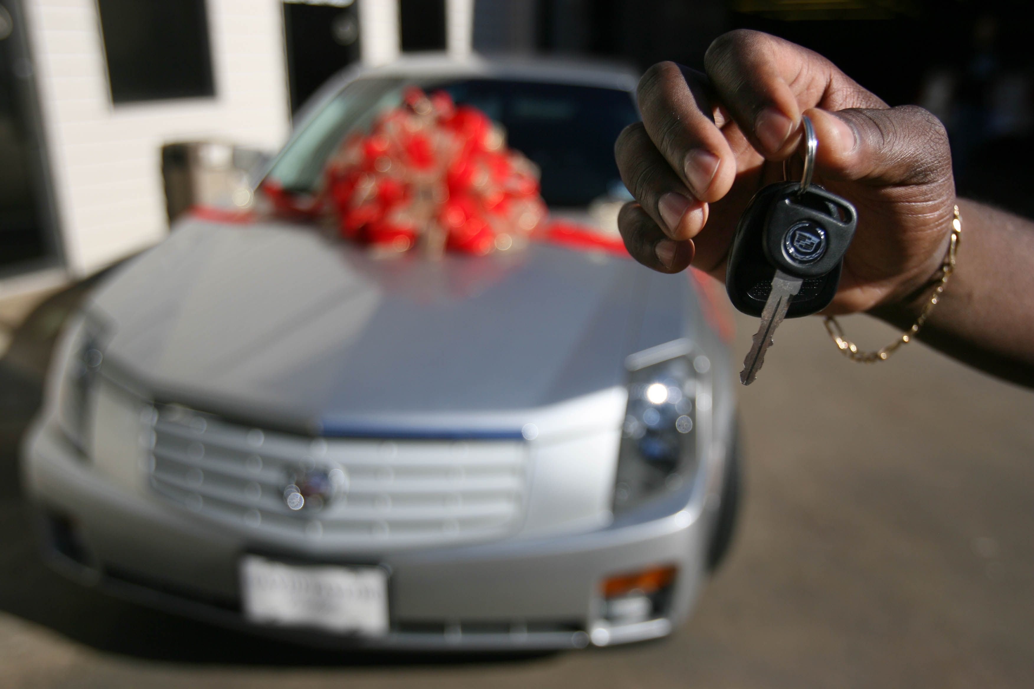 Person holding car keys in front of a luxury car with a large bow on the hood, symbolizing gift or purchase excitement