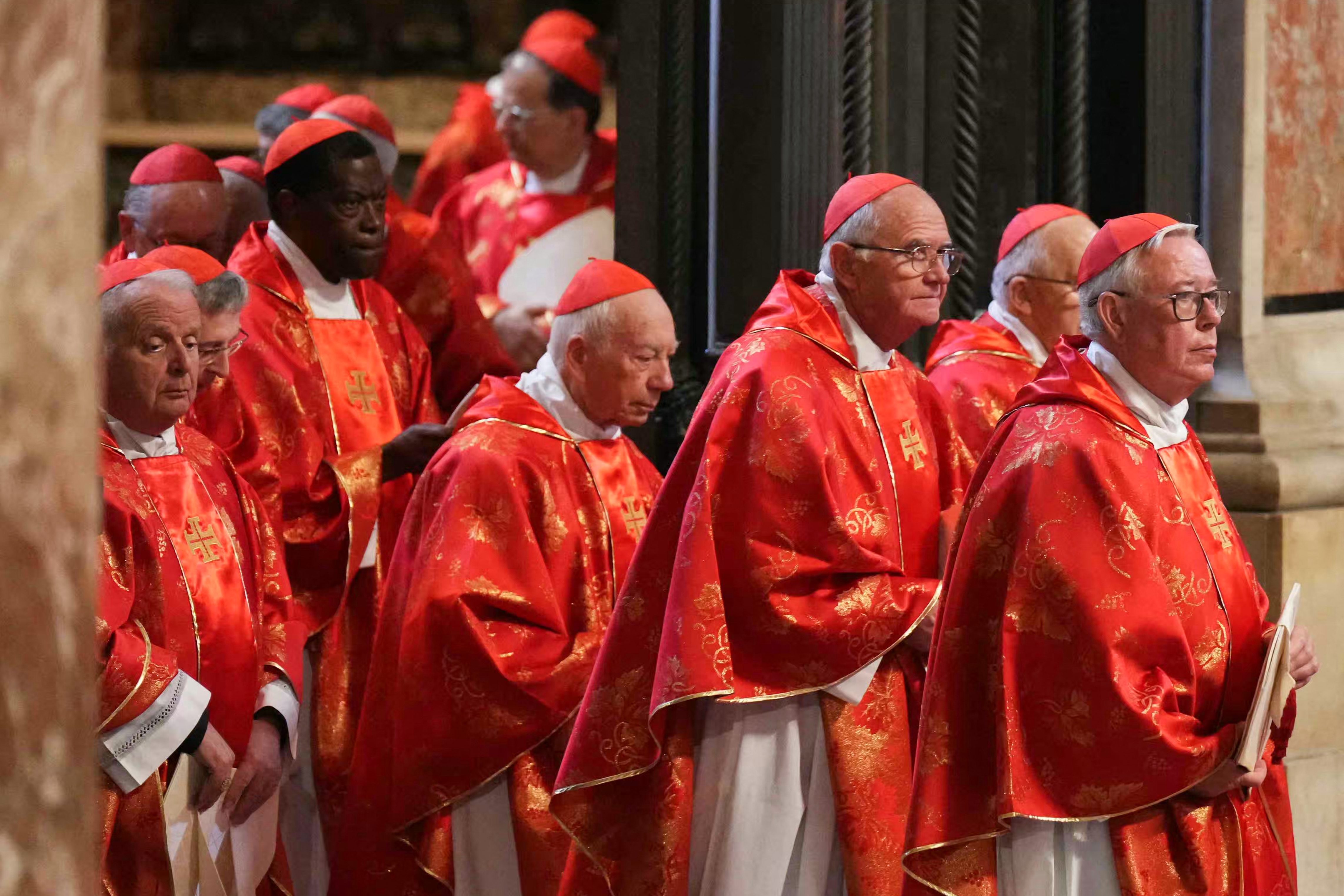 A group of clergy in ornate robes stand solemnly during a religious ceremony