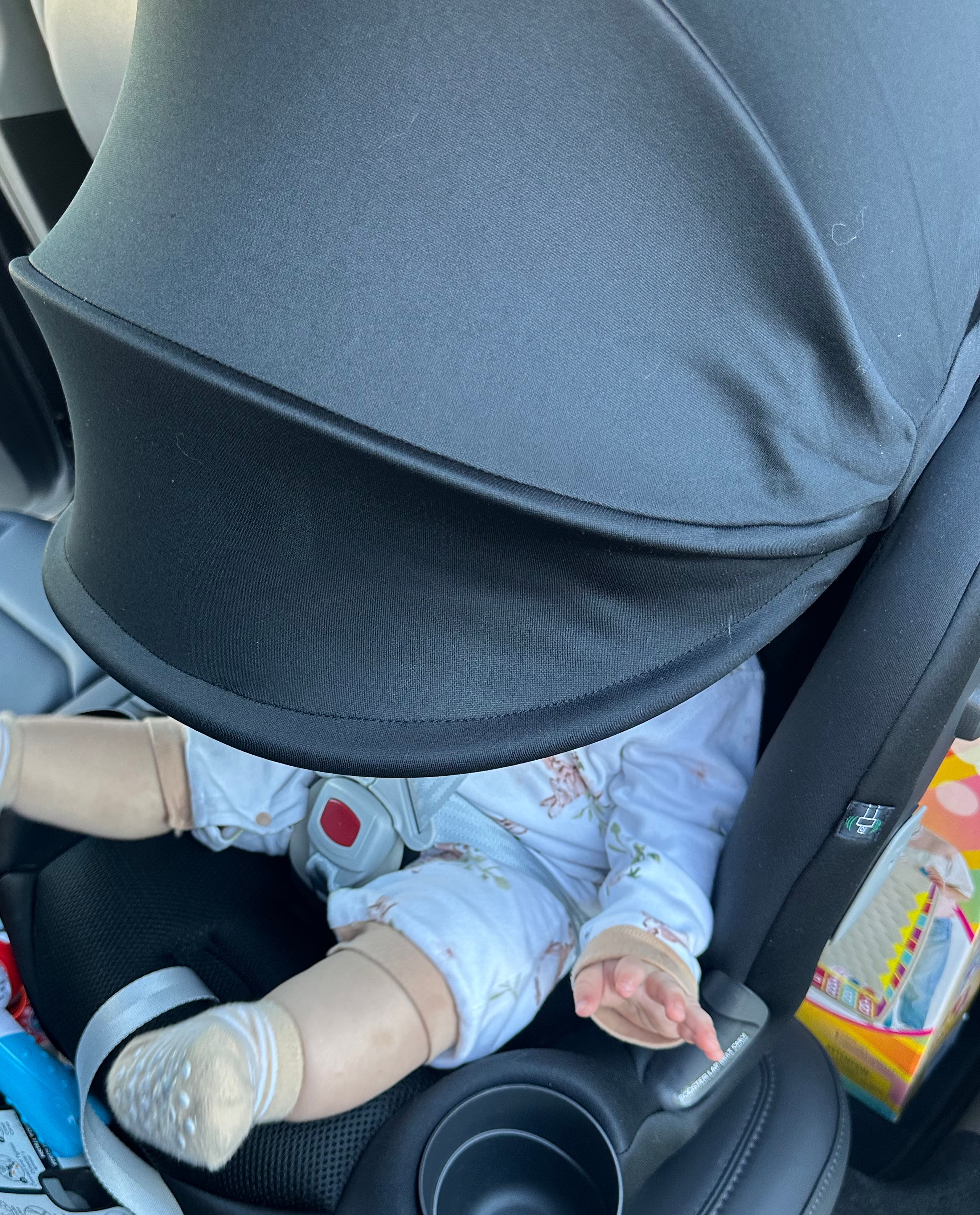 A baby in a car seat with a large sunshade covering most of their body; toy items are nearby