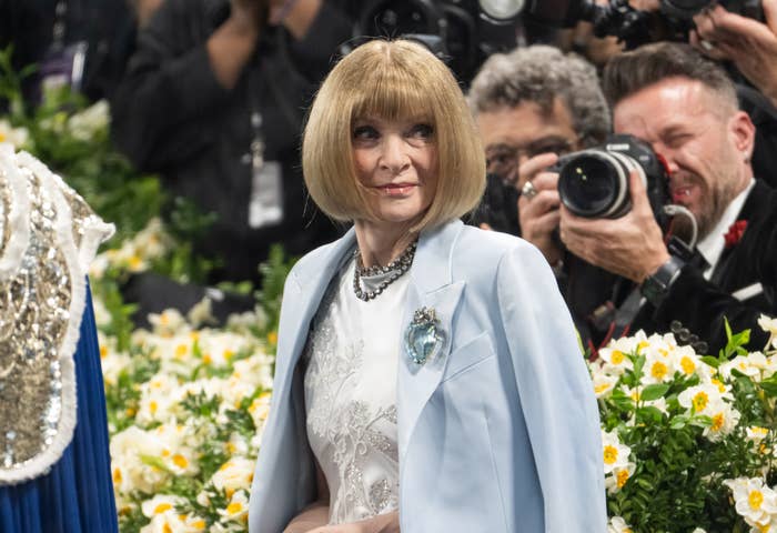 A person in elegant attire with a bob hairstyle is on the red carpet, surrounded by photographers