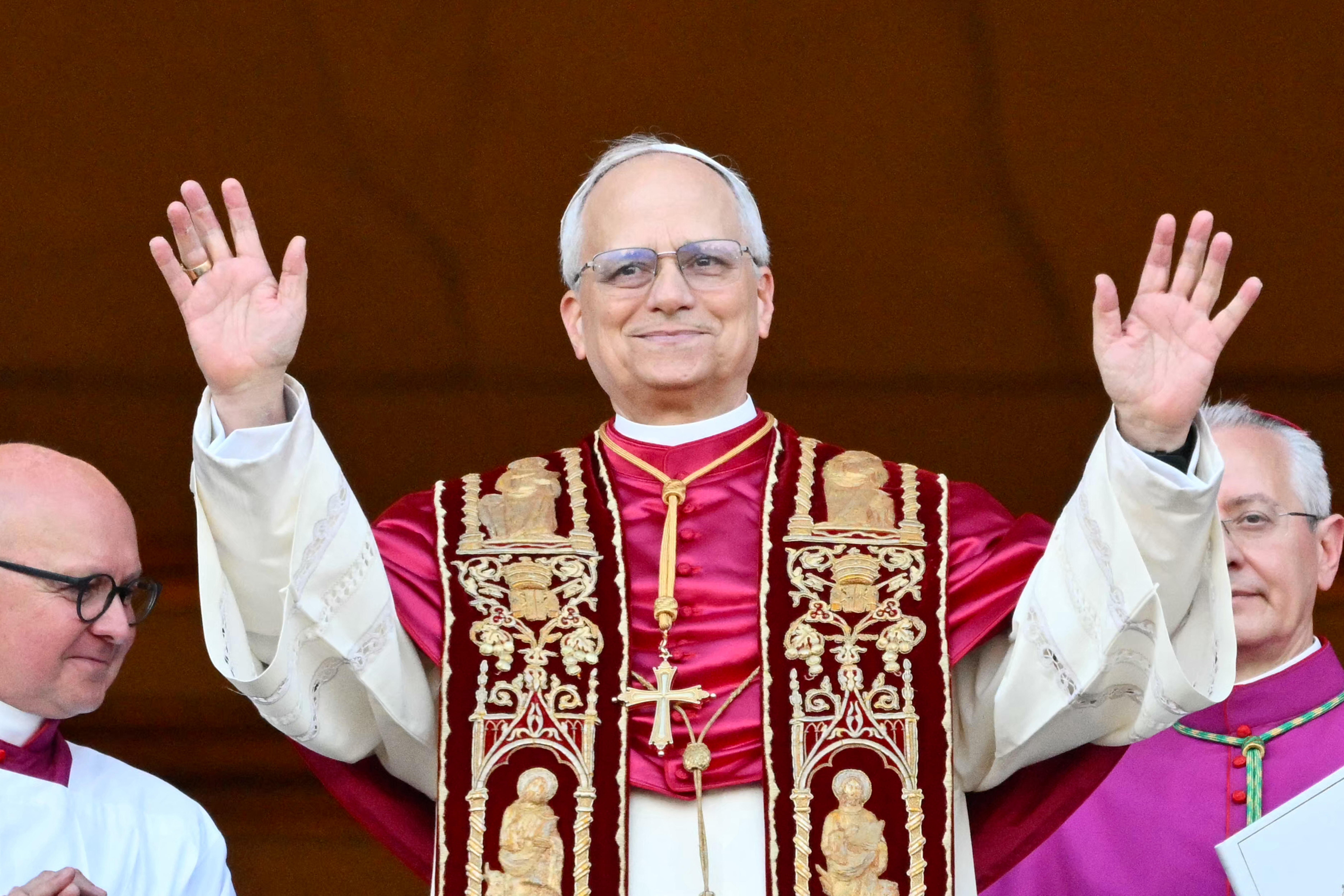 Smiling religious leader in ornate robe raises hands, standing with clergy