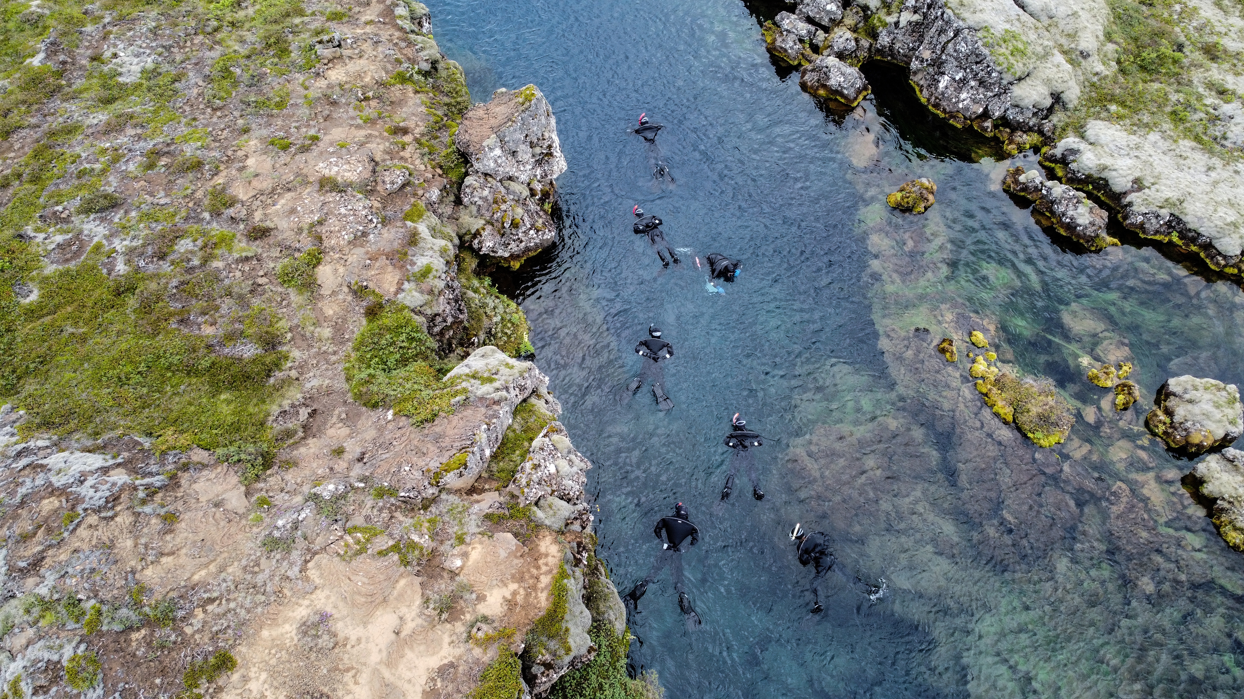 People snorkeling between tectonic plates in clear water, surrounded by rocky landscape