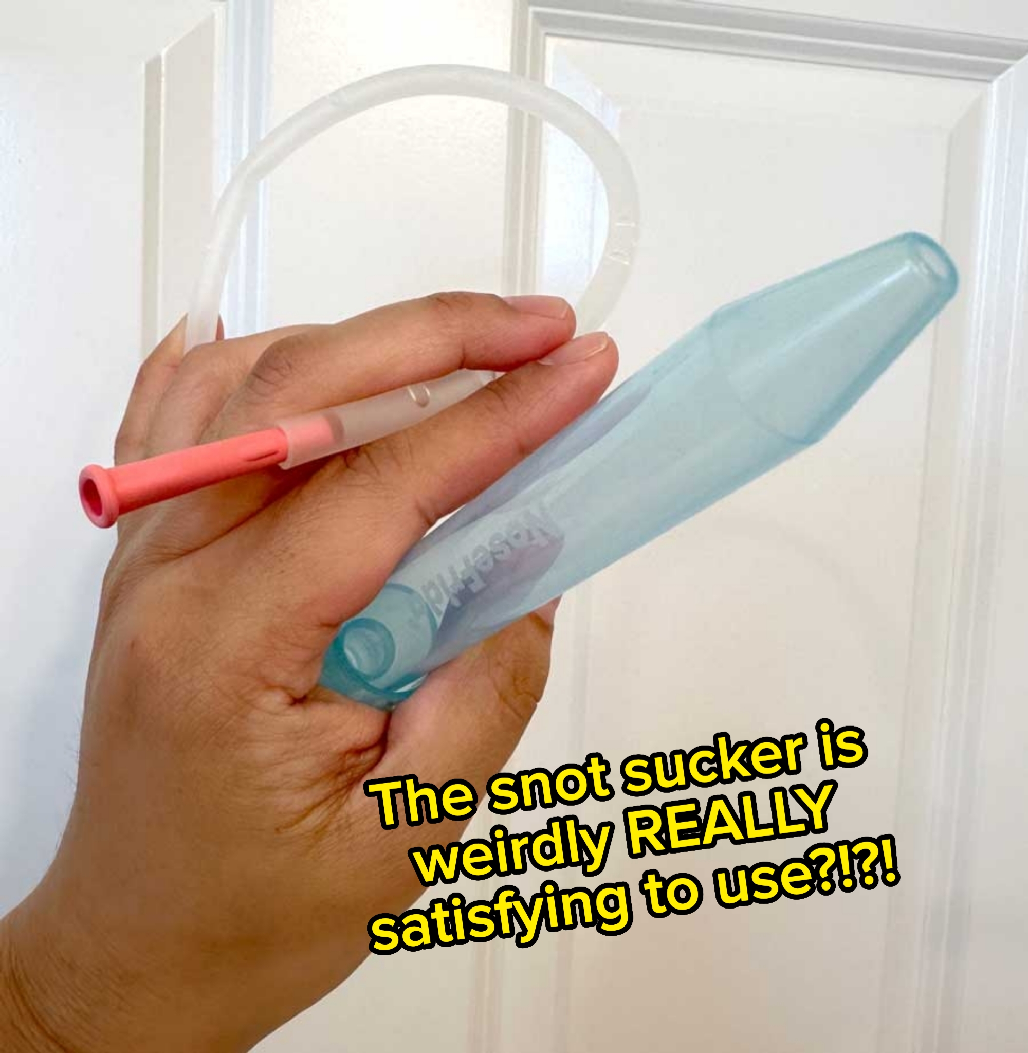 A hand holds a nasal aspirator and tube, likely a device for clearing nasal congestion in infants or children