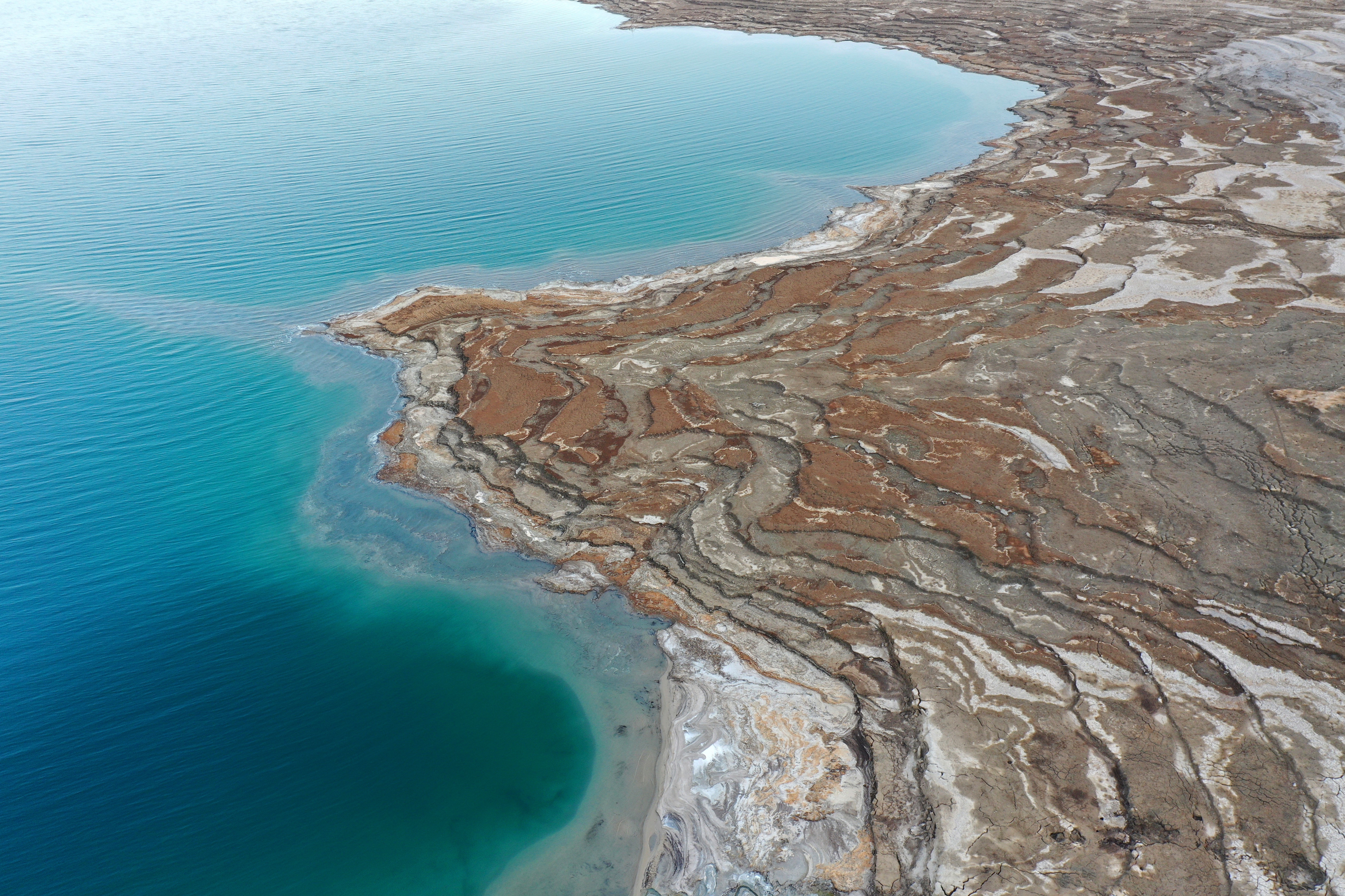 Aerial view of a rocky shoreline meeting a calm, expansive body of water, depicting natural textures and formations in a travel setting