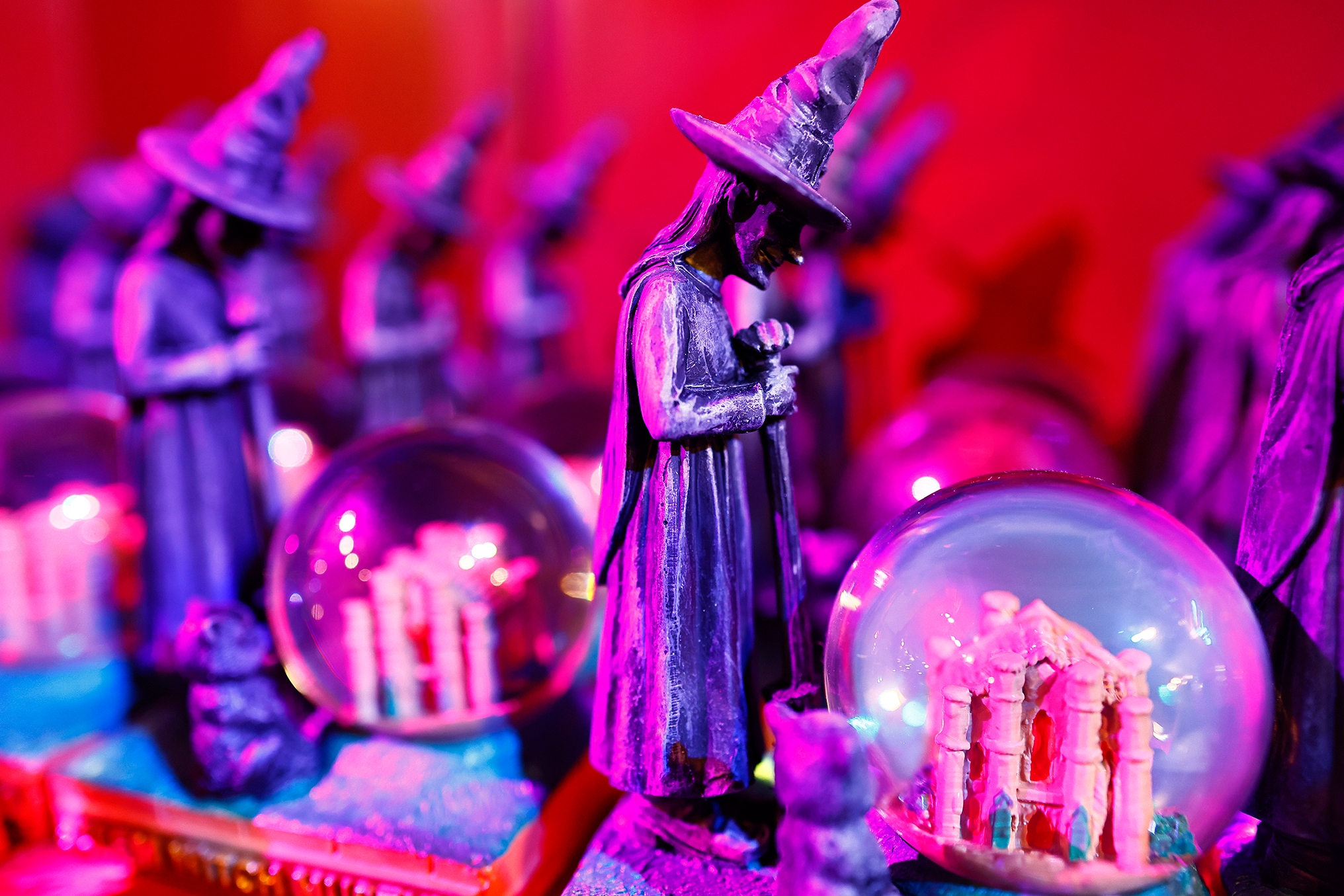 Figurines of witches with snow globes featuring miniature castles. Bright light enhances the magical theme, creating a whimsical travel souvenir scene