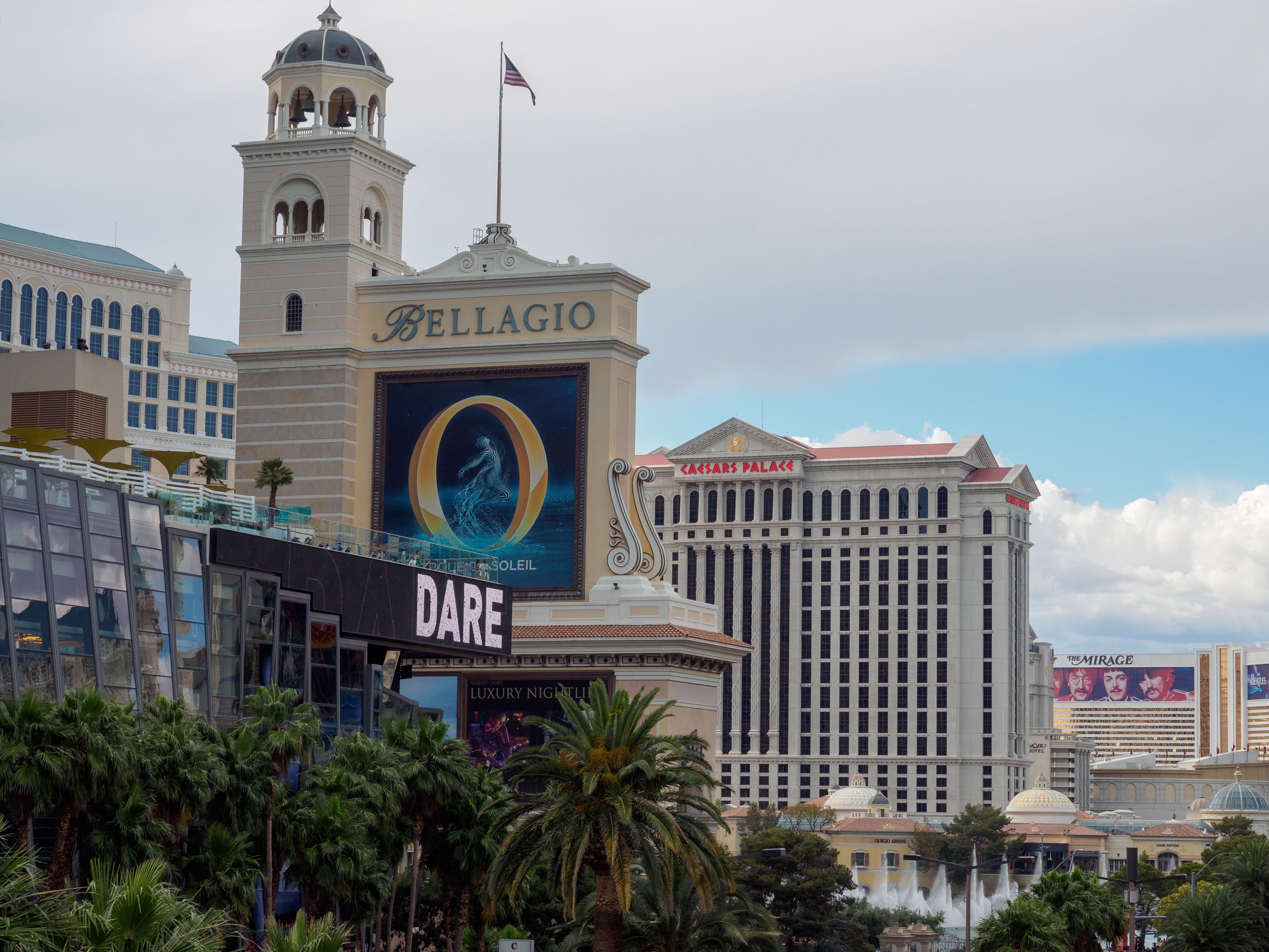 Las Vegas Strip view featuring Bellagio and Caesars Palace hotels, surrounded by palm trees and billboards