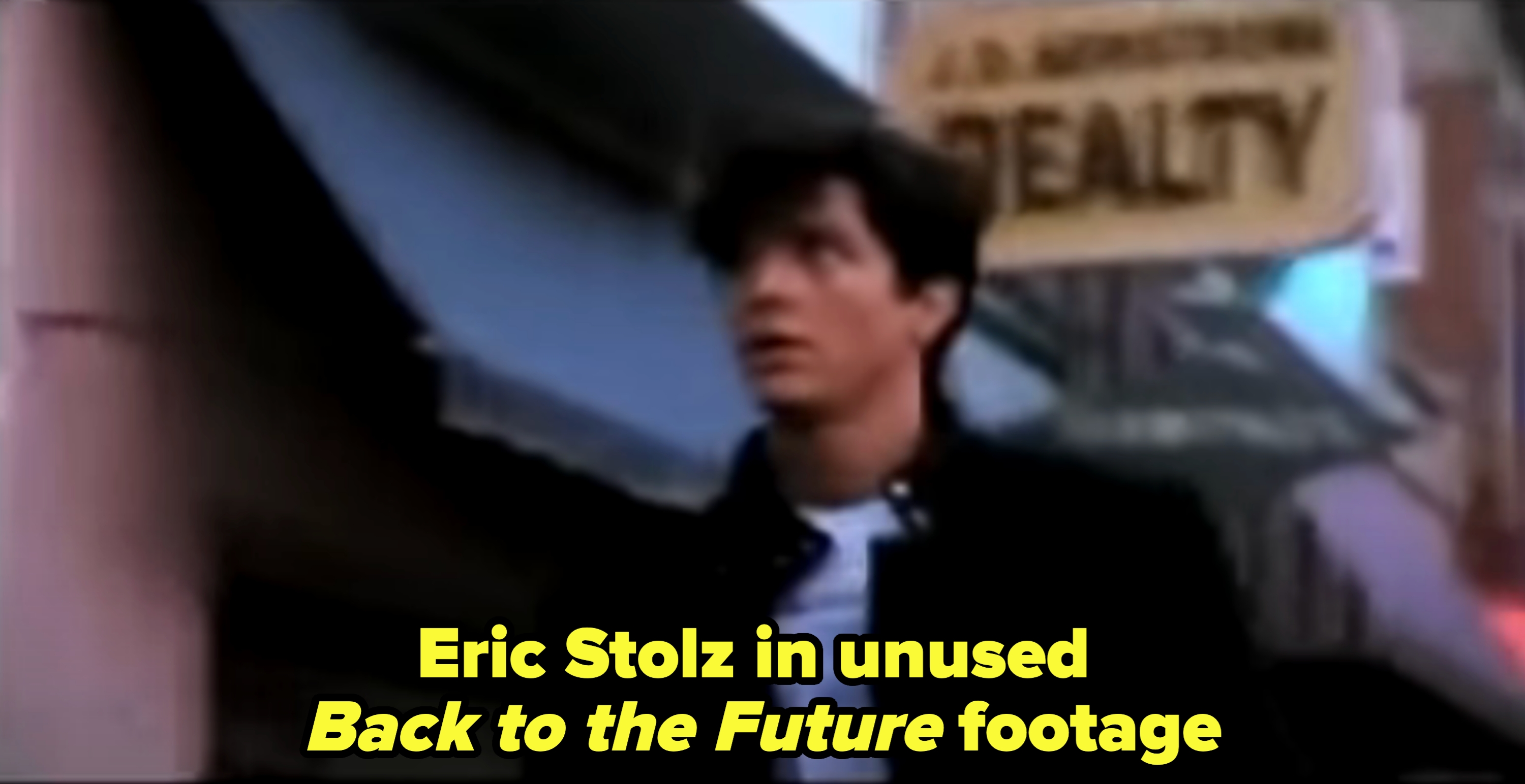 Eric in a casual jacket walks past a building, with a blurred &quot;Reality&quot; sign in the background