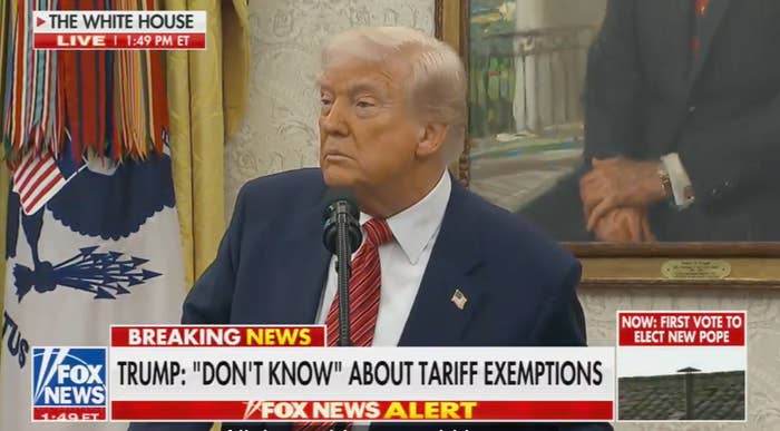 Donald Trump speaks at a podium with a microphone in a room, surrounded by flags and framed photos. News ticker text discusses tariff exemptions
