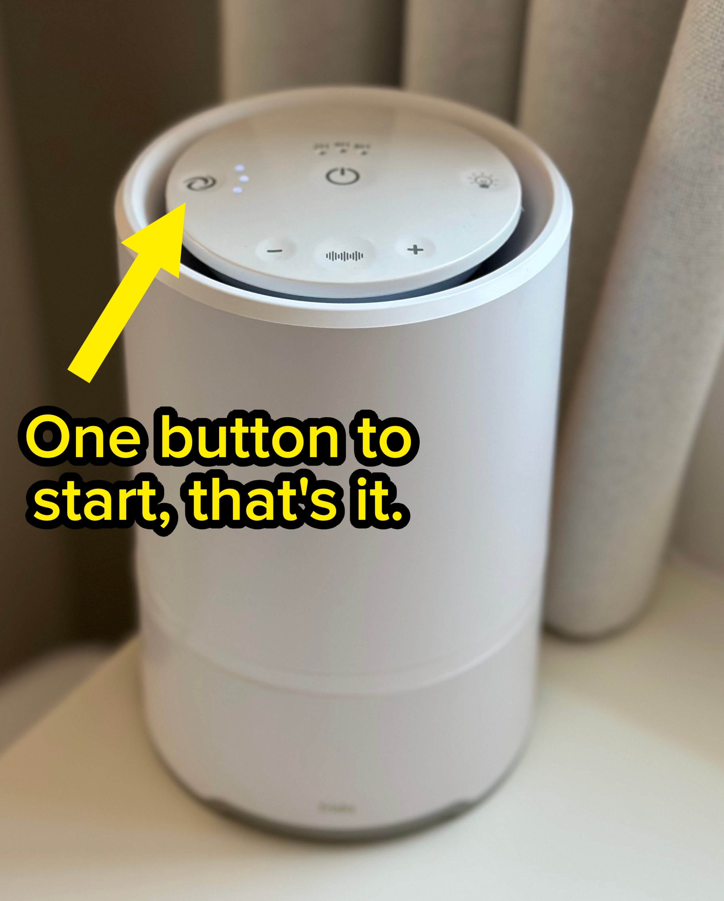 White air purifier on a table with a digital display panel on top, near a curtain backdrop