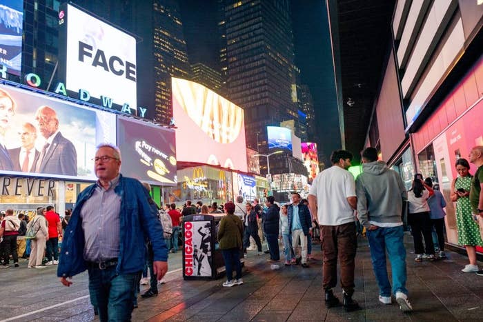 Crowds of people walk in Times Square, New York at night, surrounded by bright digital billboards and bustling city energy