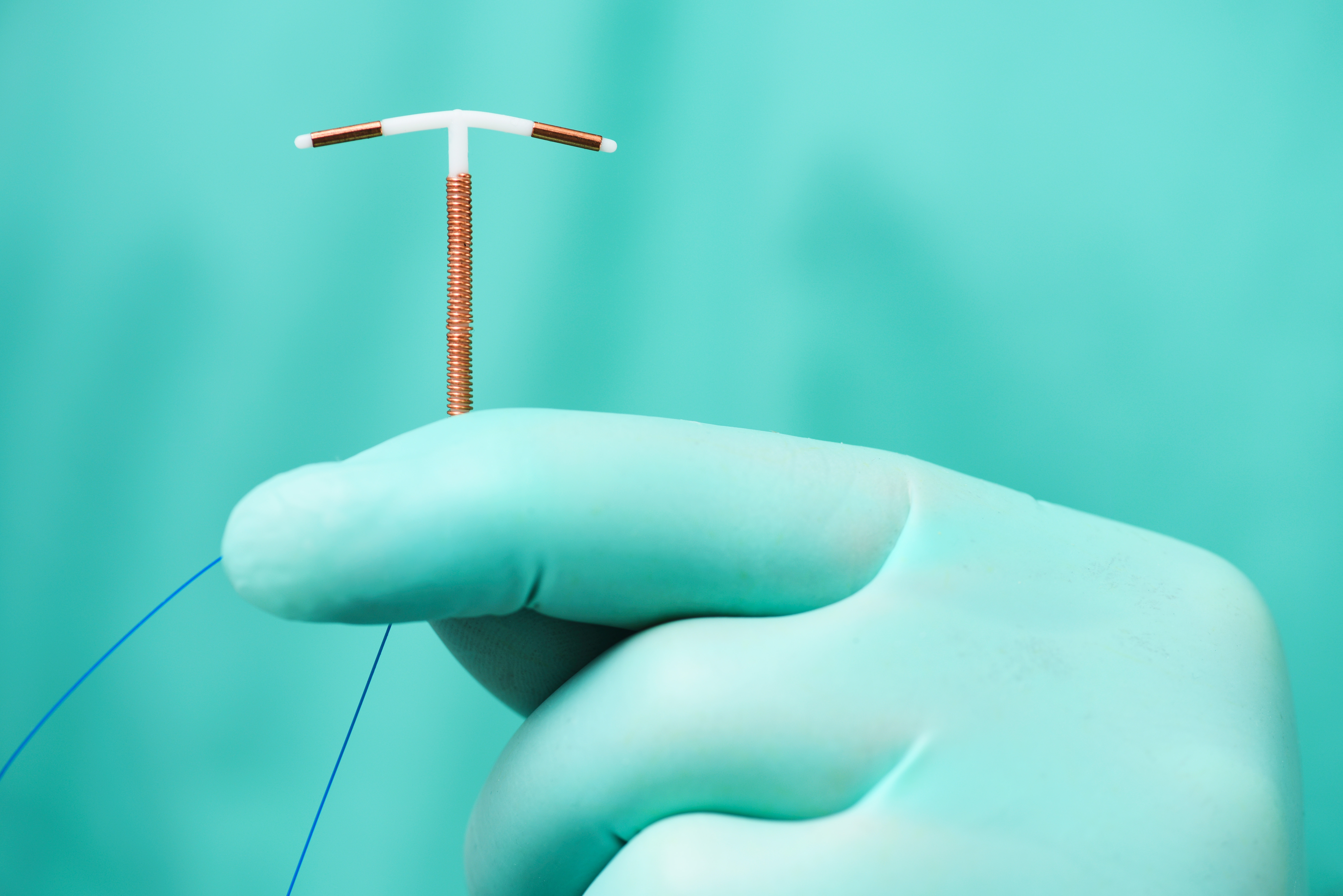A gloved hand holds an IUD, a small T-shaped contraceptive device