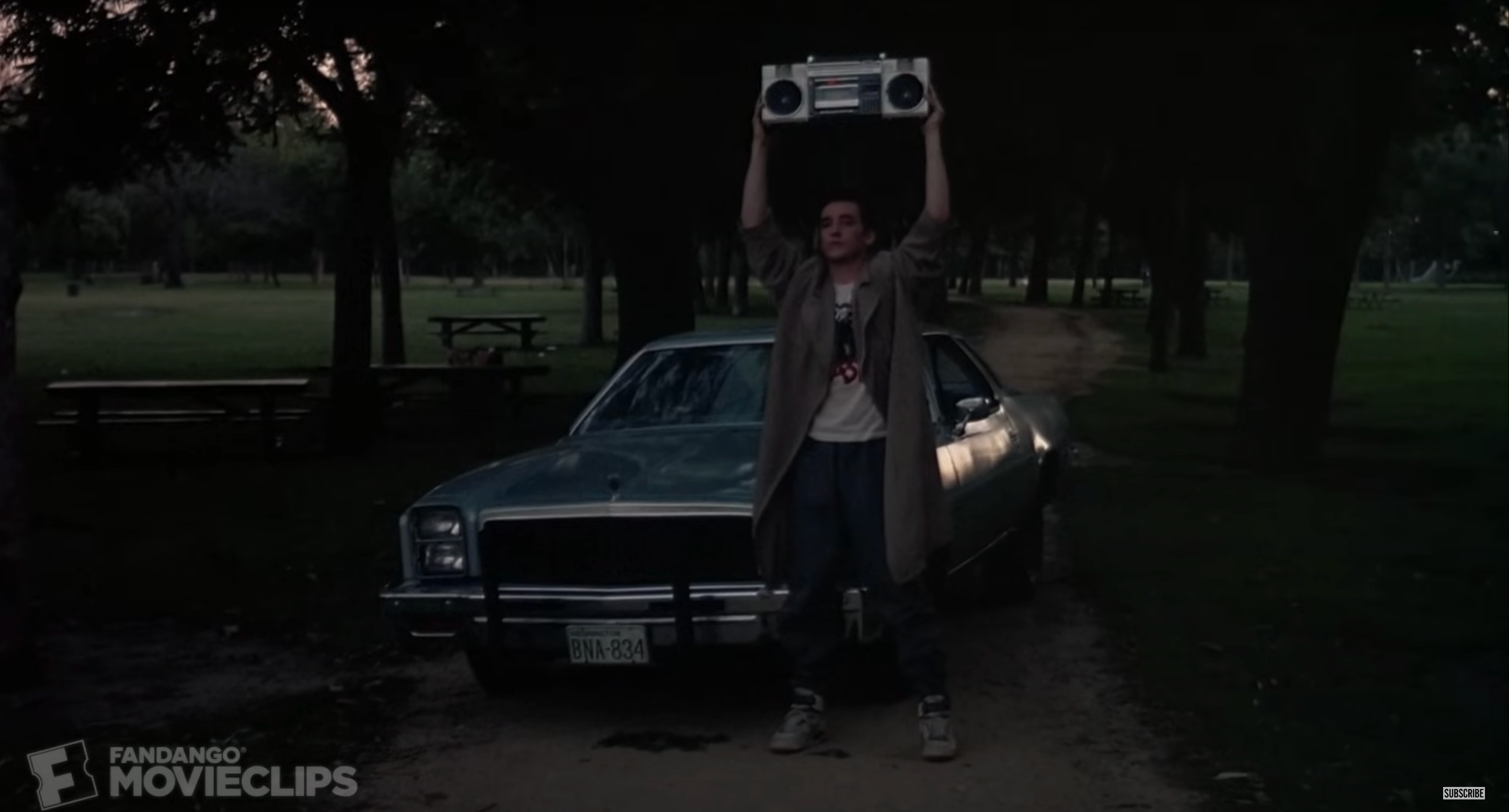 John holding a boombox over his head in front of a car