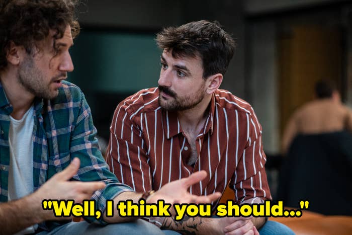 Two men are engaged in a serious conversation indoors. One wears a plaid shirt, and the other has a striped shirt