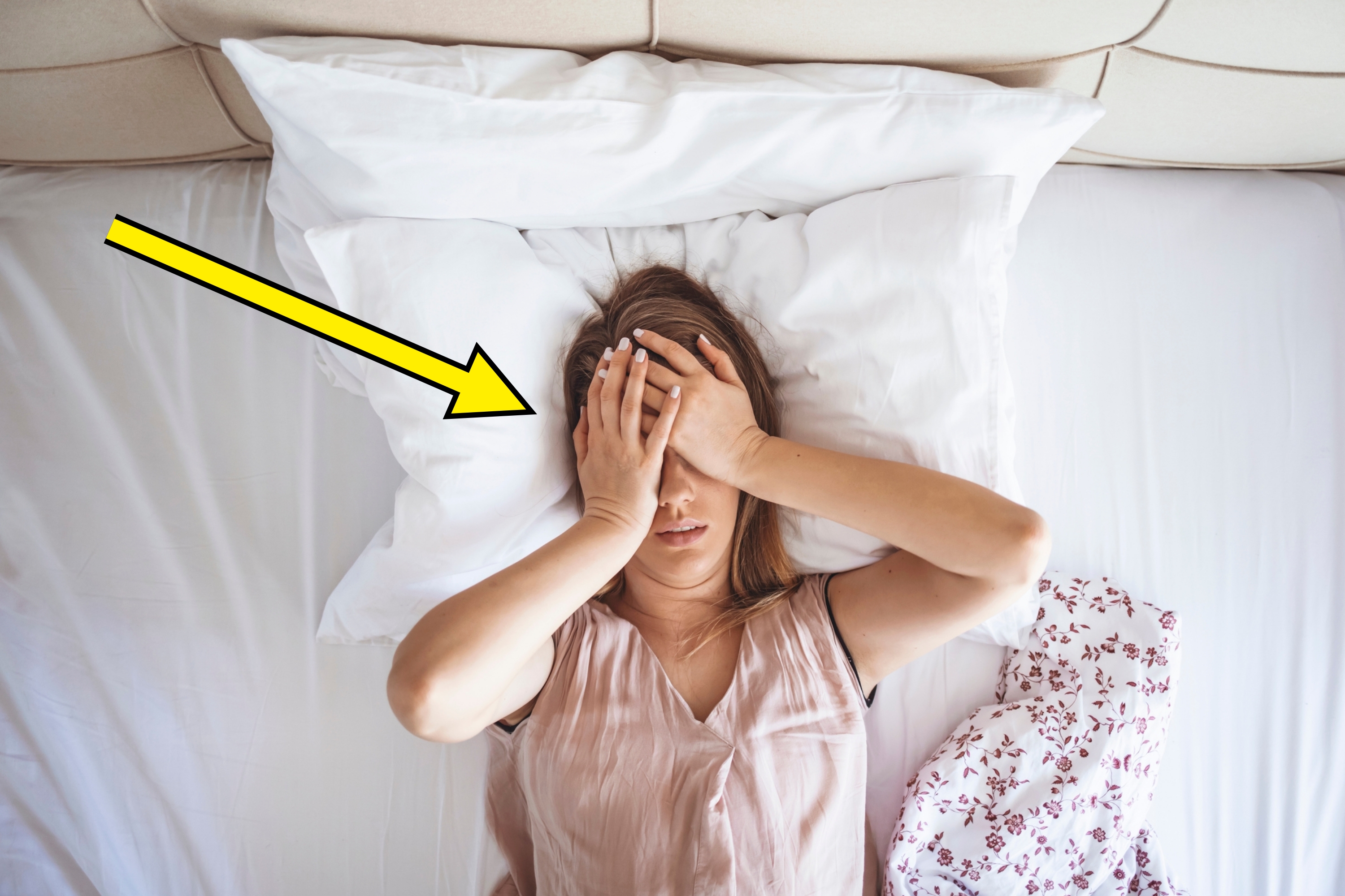 Person lying on a bed with hands covering their face, appearing stressed or overwhelmed