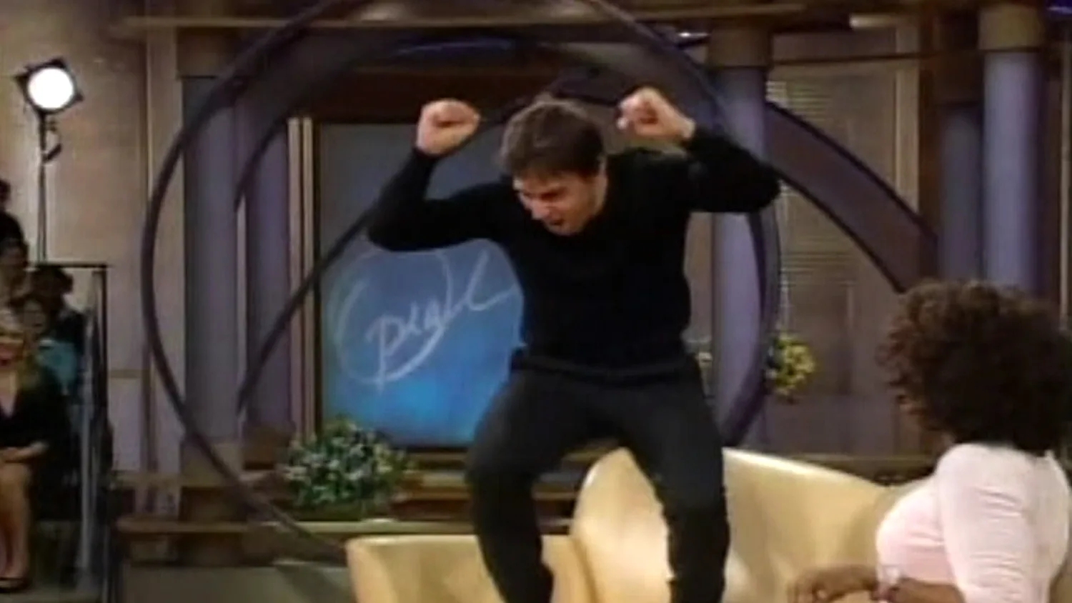 Person energetically jumping on a talk show couch, gesturing with excitement toward the host seated nearby