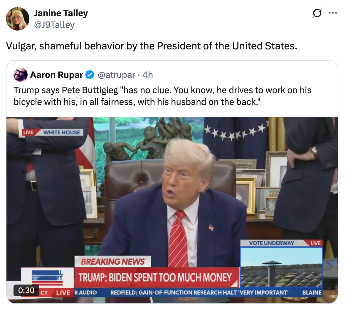 Video still of a news clip with Trump speaking, sitting at a desk during a press event, surrounded by flags and framed photos