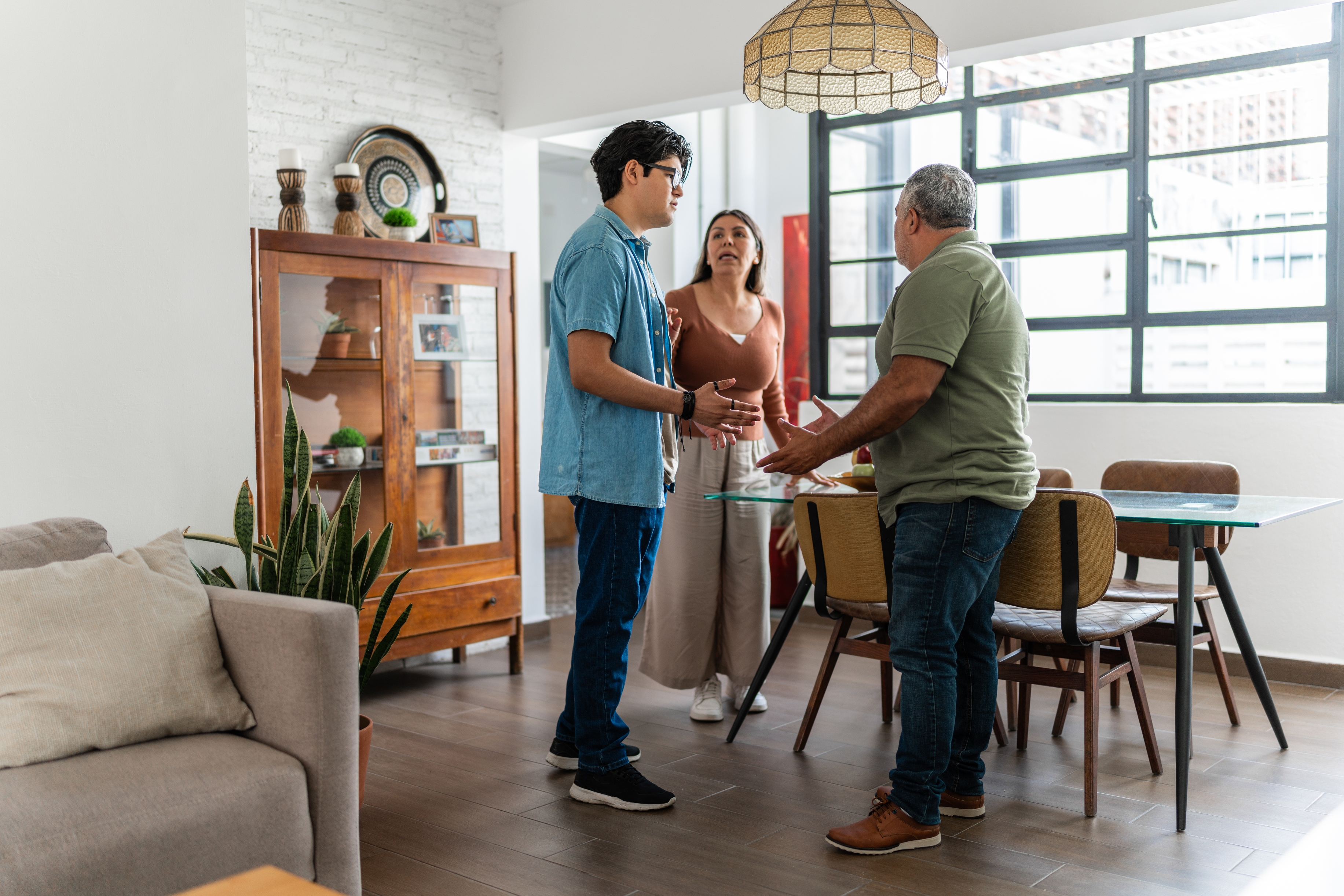 Three adults in a modern living room engage in a heated discussion, gesturing expressively with serious expressions