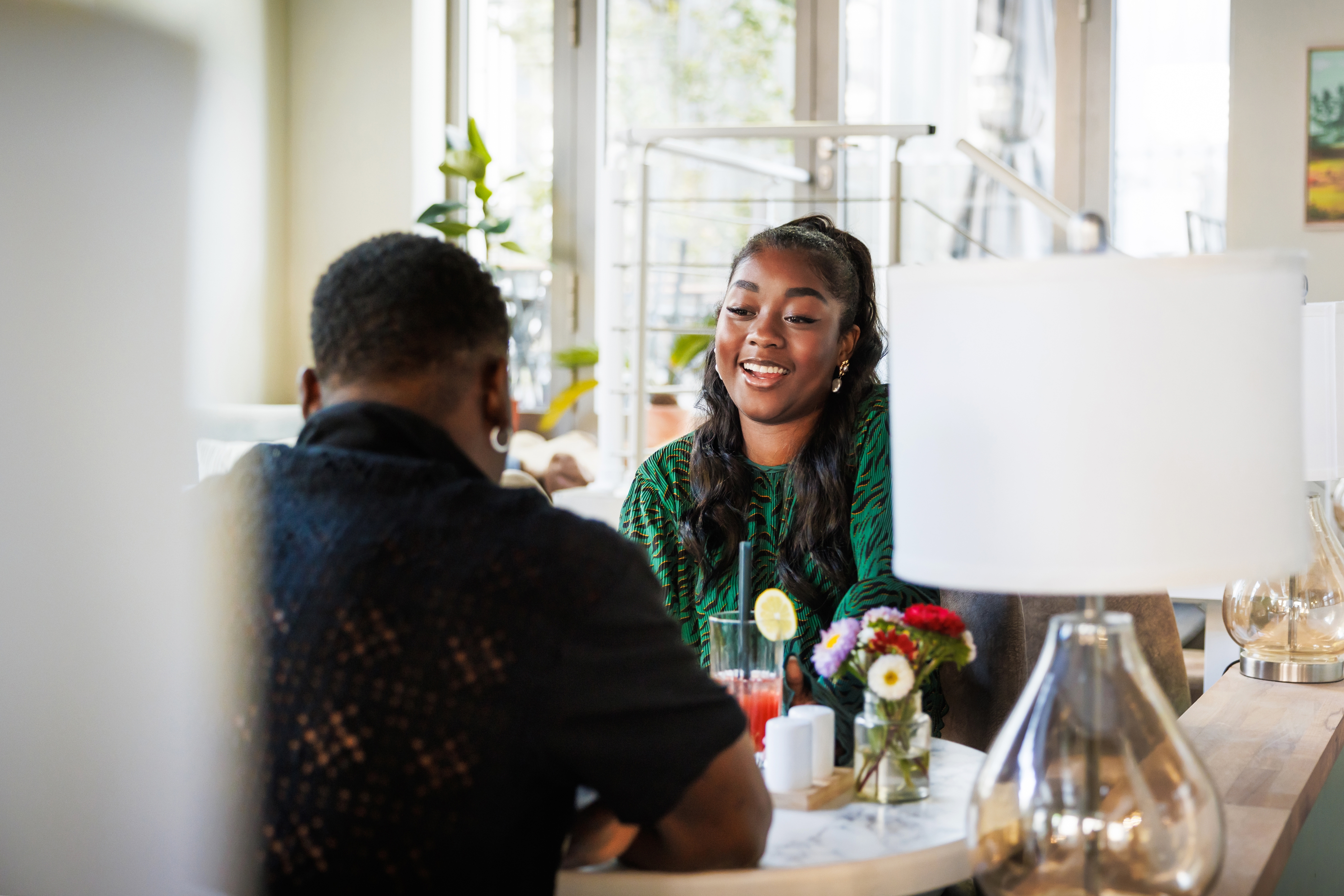 Two people smiling and chatting at a cozy cafe table with drinks and small flower arrangements