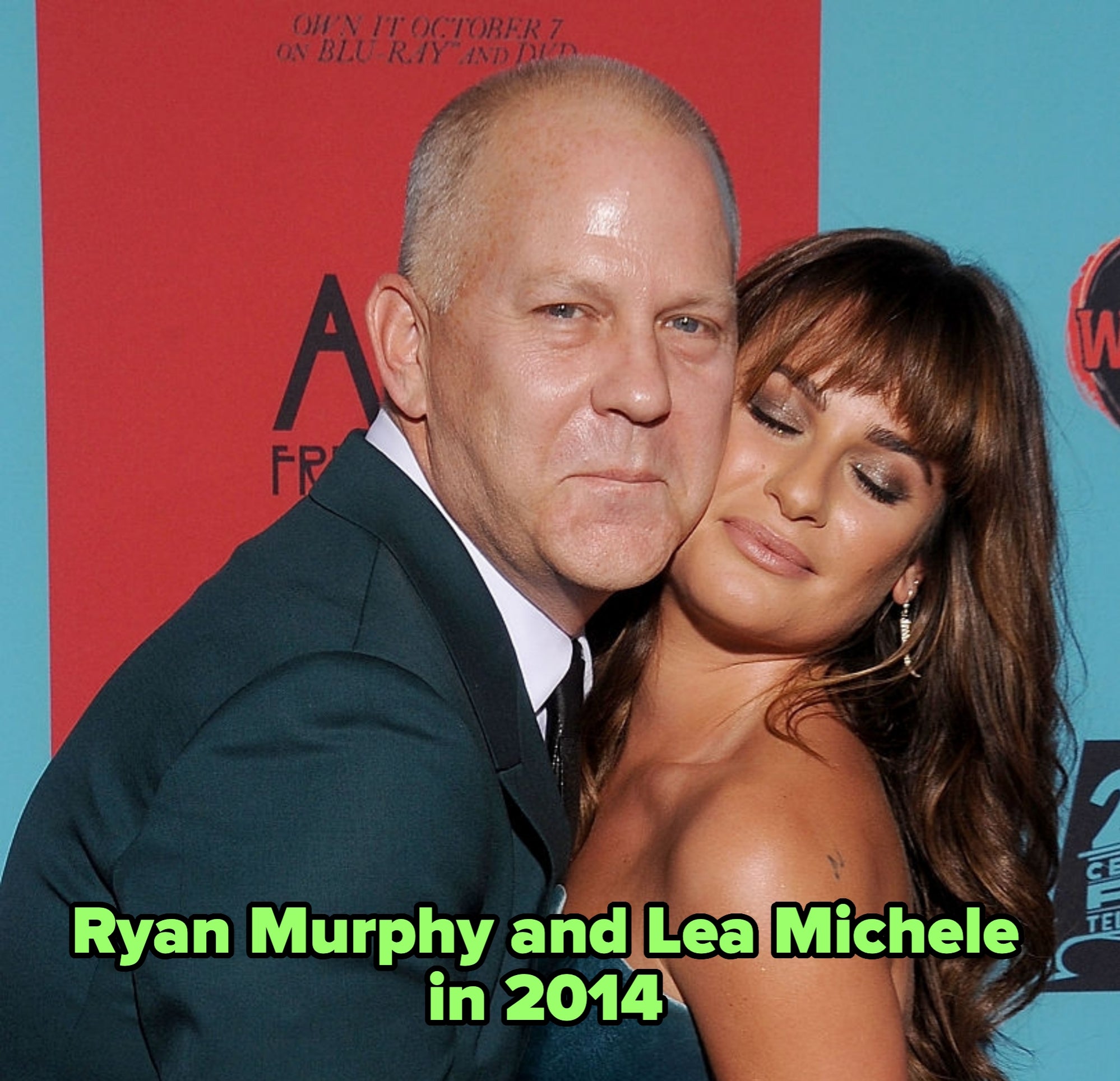 Two people embracing at an event. The person in a suit has a serious expression, while the other person wears a strapless gown and appears content