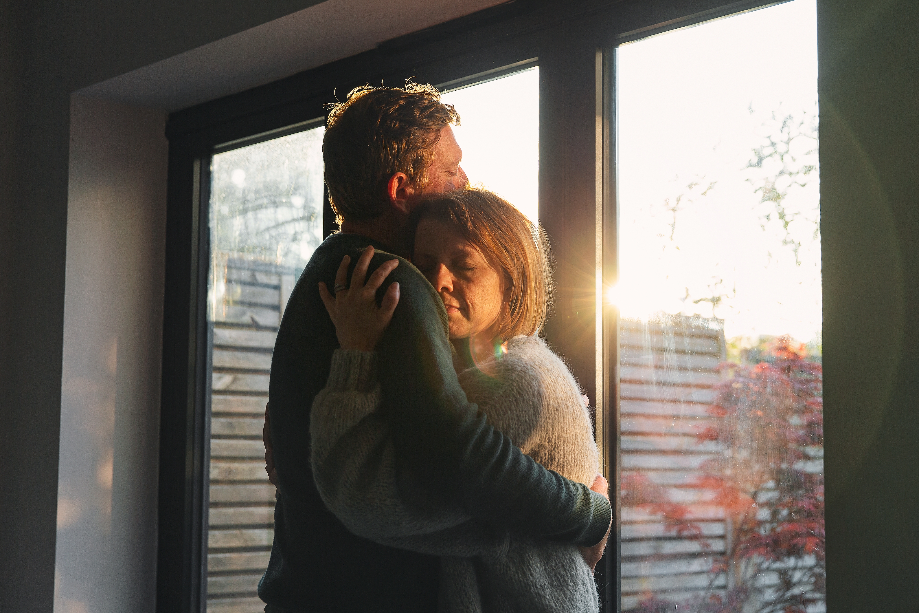 A couple embraces tenderly by a sunlit window, creating a warm, comforting moment of connection and peace