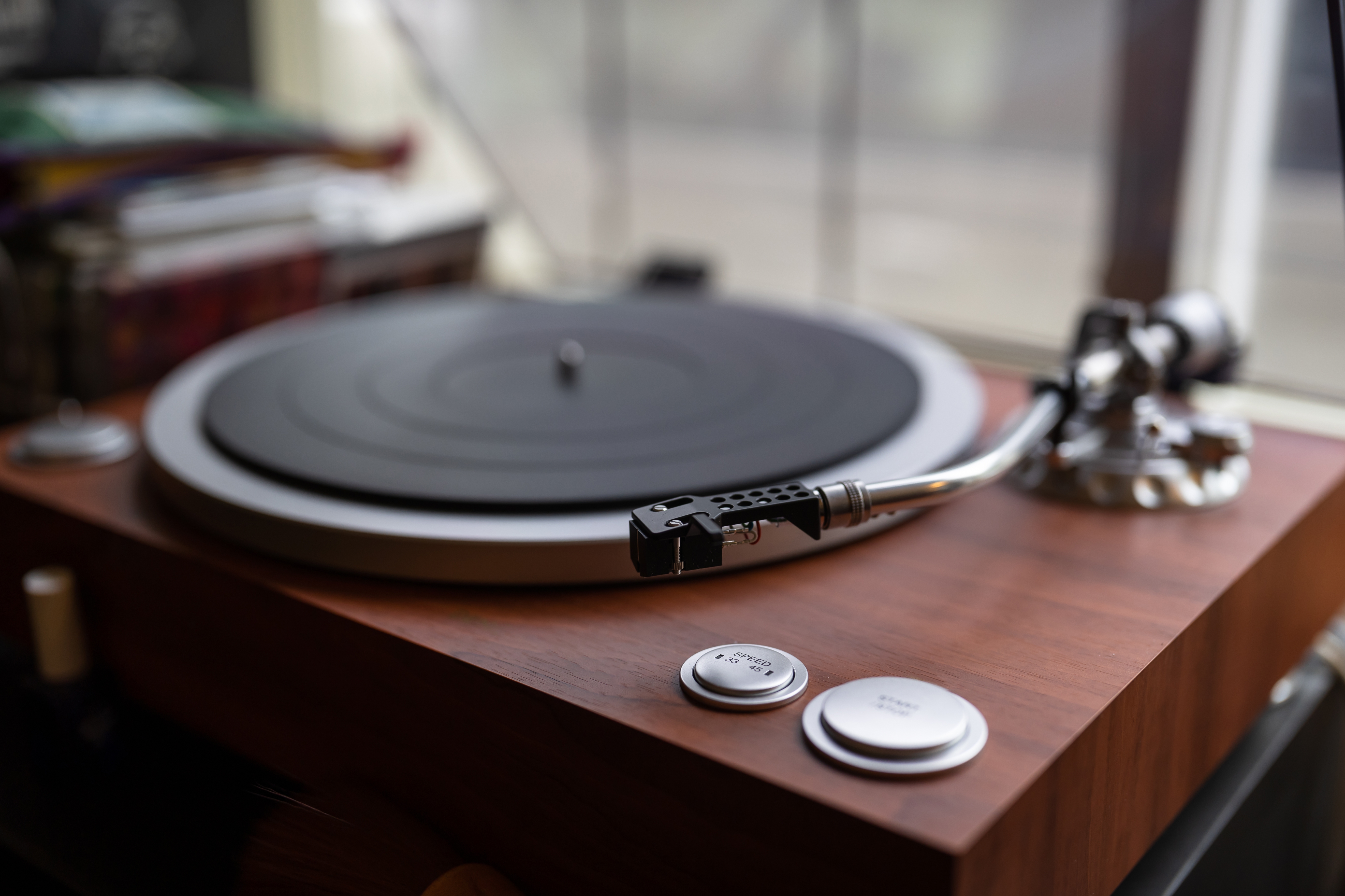 A close-up of a vintage turntable with a vinyl record on it, emphasizing the tonearm and controls, in a well-lit room