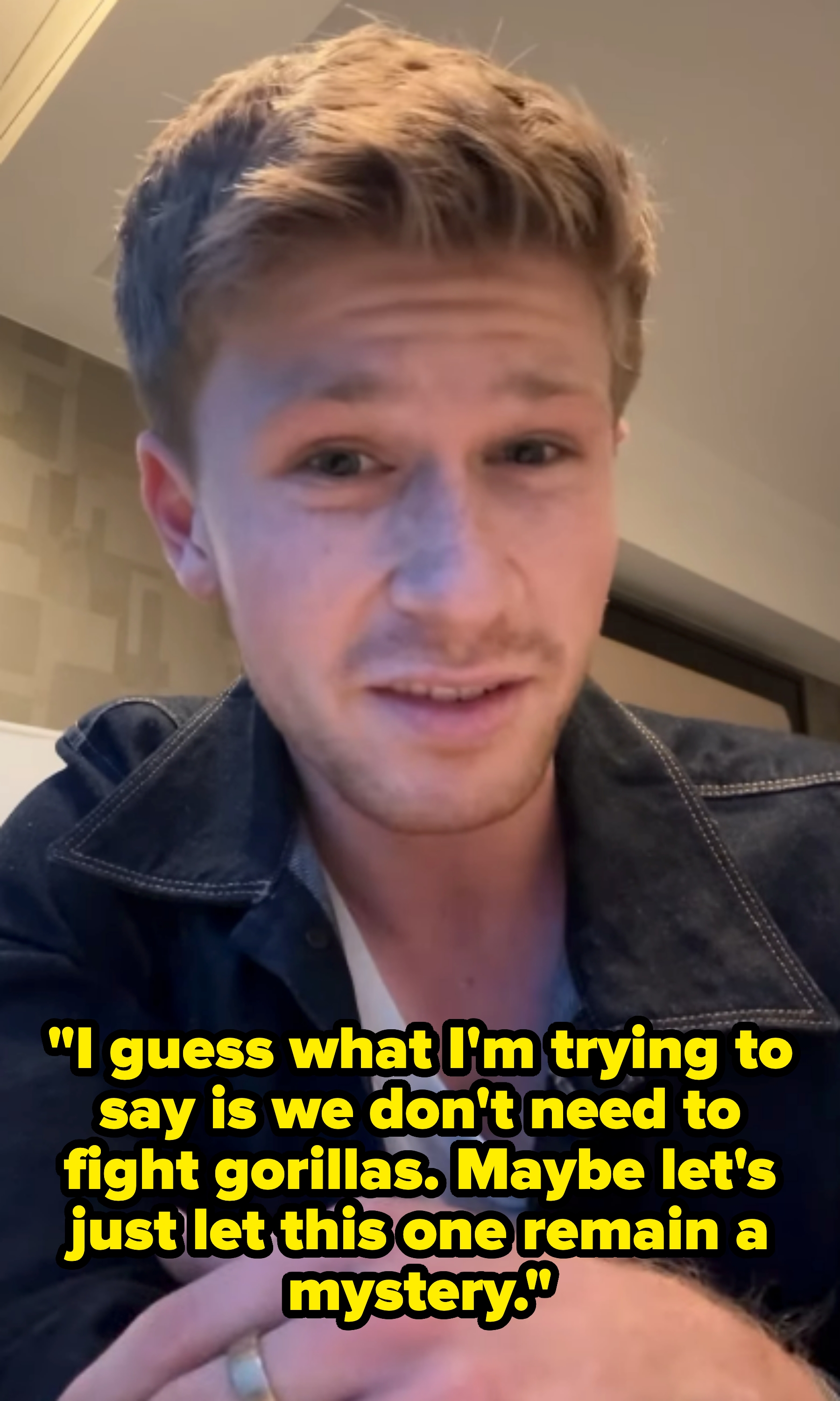 Person in a casual setting wearing a black denim jacket over a white shirt, looking at the camera