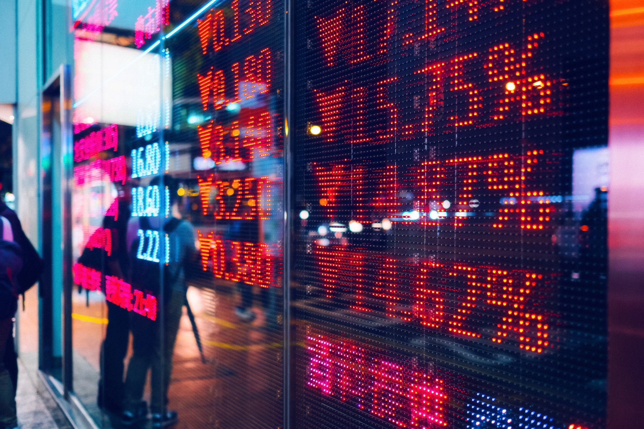 Stock market board displaying fluctuating numbers and percentages, indicating active financial trading activity in a bustling urban environment