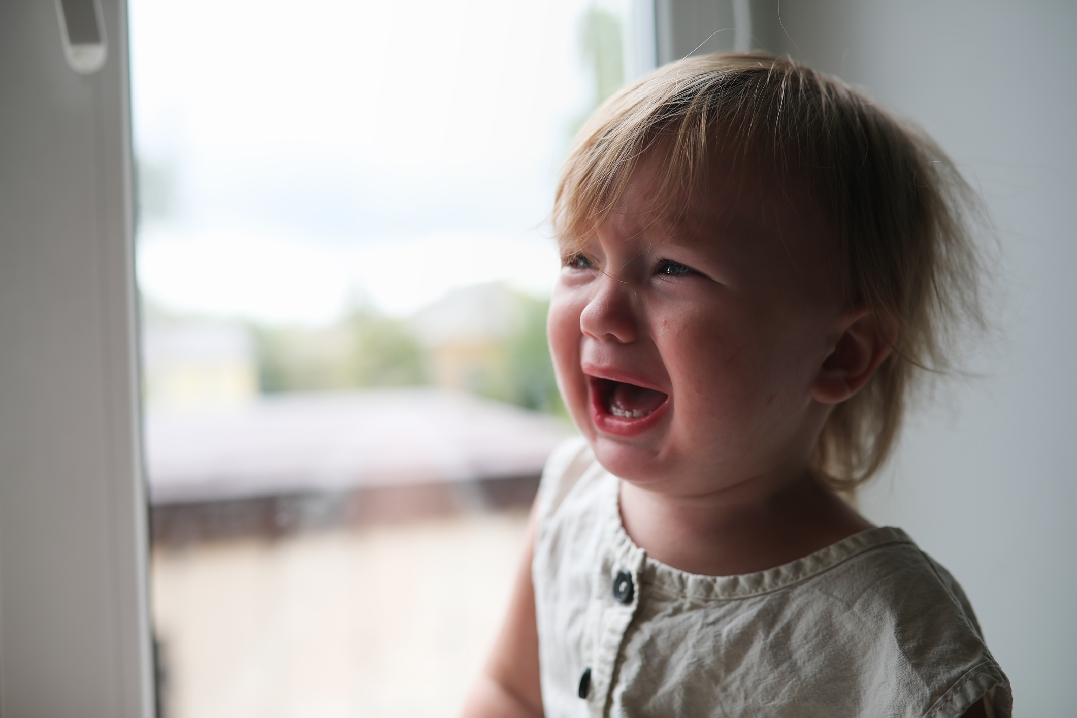 Toddler standing by a window, crying with an open mouth