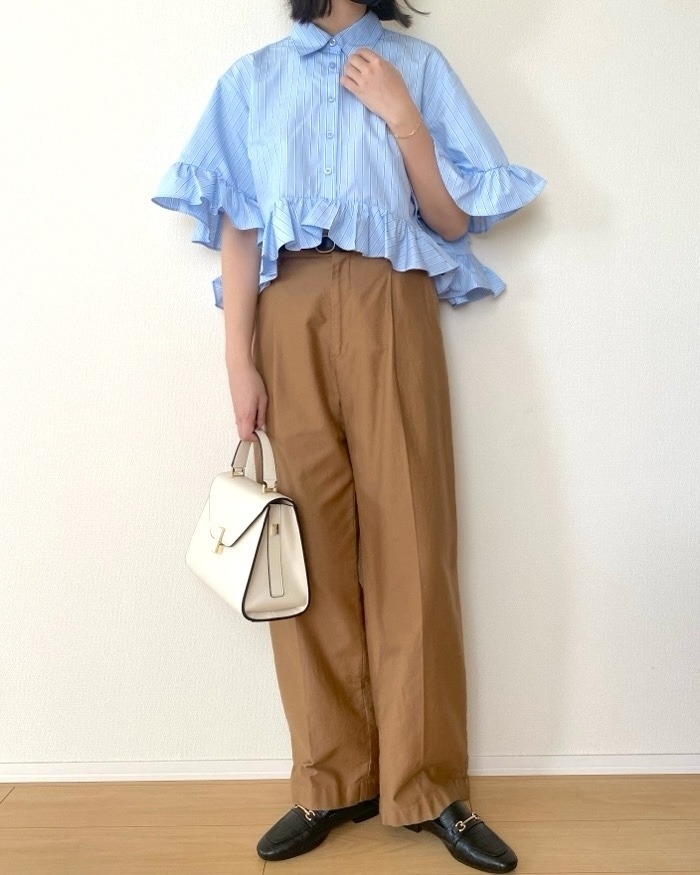女性がフリル付きシャツとワイドパンツを着て、白いバッグを持っている。