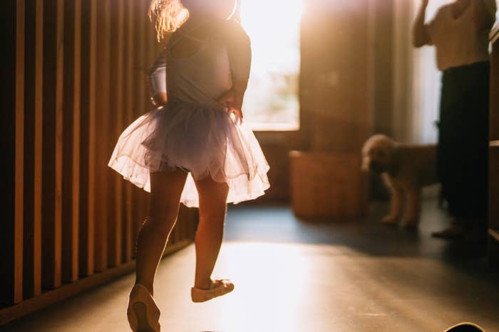 Child in ballet outfit joyfully runs inside a sunlit room, creating a warm and playful atmosphere
