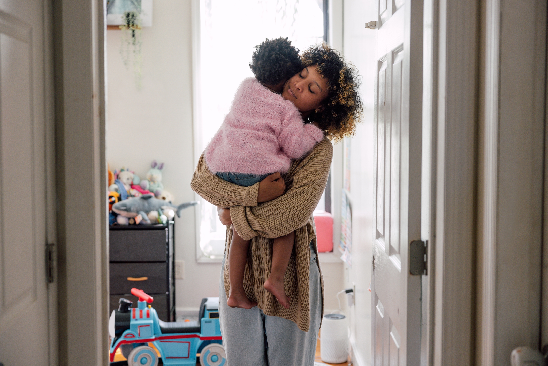 Parent gently holds and comforts a child in a cozy room with toys visible in the background