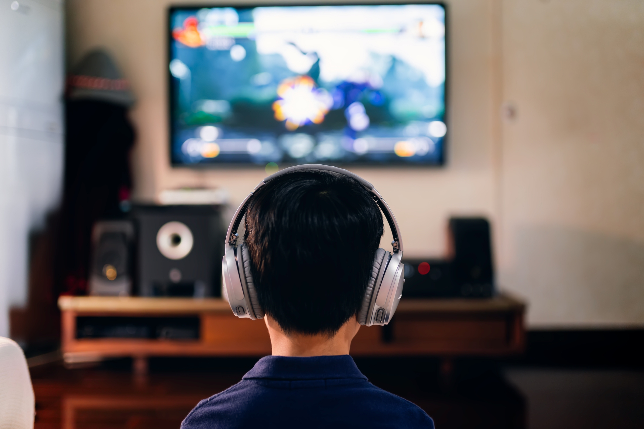 A child wearing headphones sits facing a TV screen displaying a video game in a living room setting