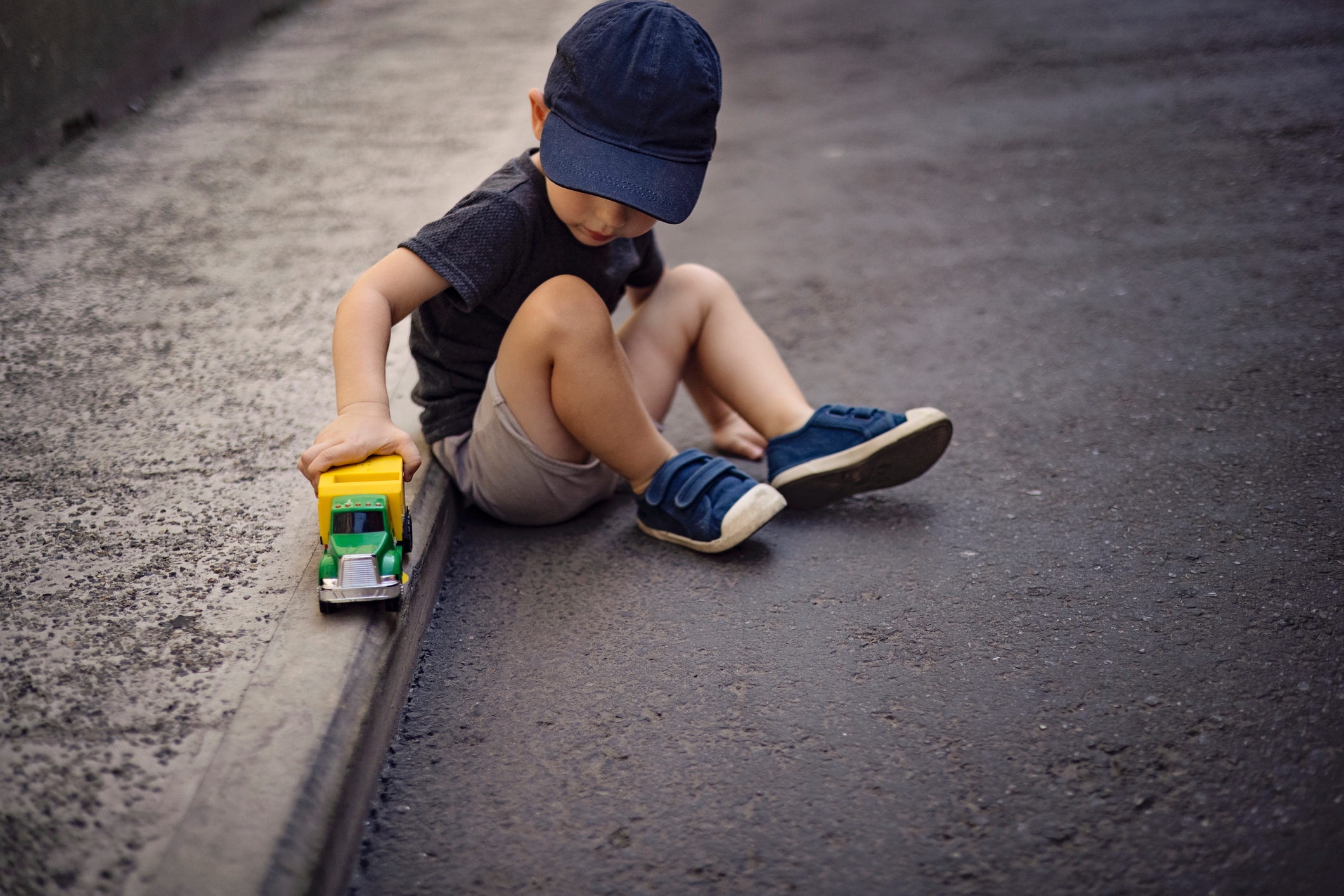 Young child in casual clothing plays with a toy truck on the pavement, focused on the activity