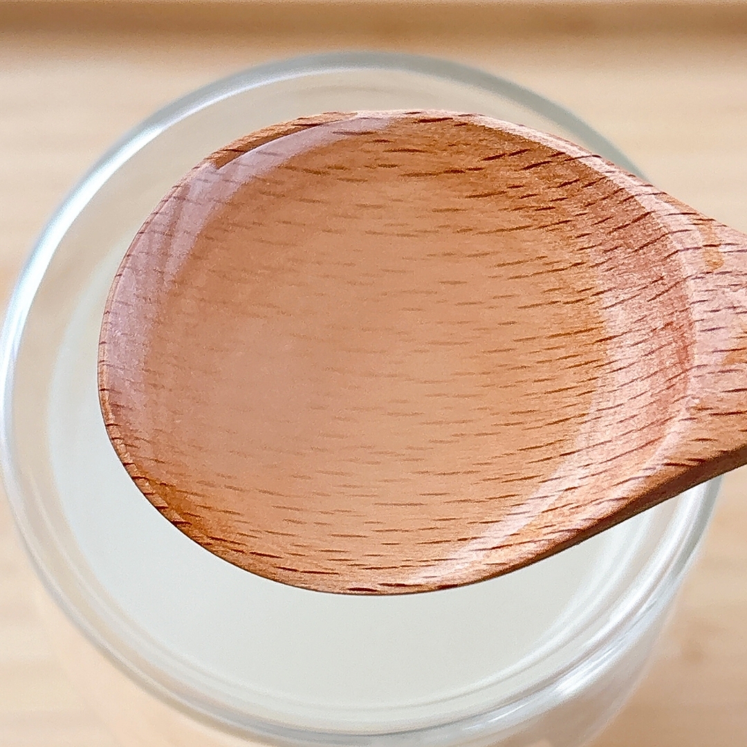 ガラス容器に入った白い液体をすくう木製のスプーン。