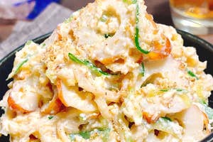 クリーミーなポテトサラダにキュウリとニンジンのスライスが混ざった料理が黒いボウルに盛られている。