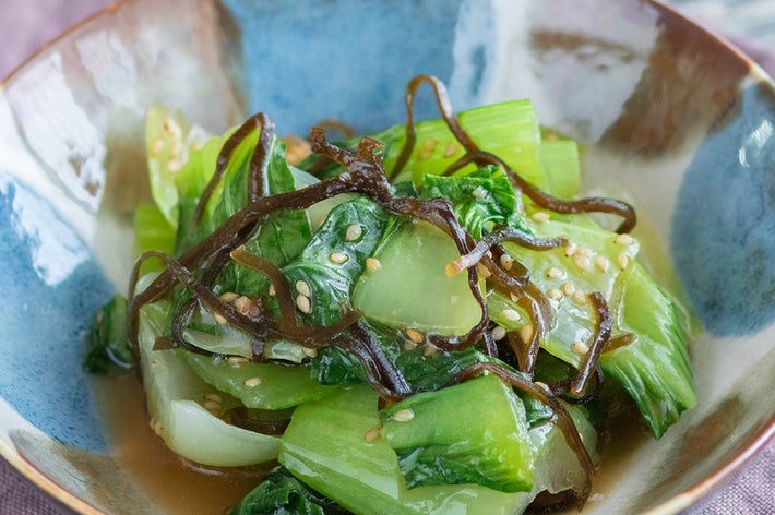 器に盛られた青菜の煮物。ゴマと昆布がトッピングされている。