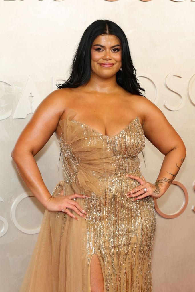 Person in an elegant, strapless gown with sequins and tulle detail poses confidently on a red carpet