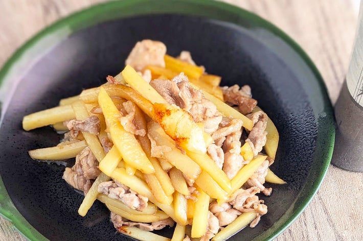 皿に盛られたじゃがいもと豚肉の炒め物。テーブルに箸が置かれている。