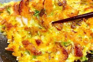 皿に盛られた美味しそうなオコノミヤキが、箸で一口掴まれています。