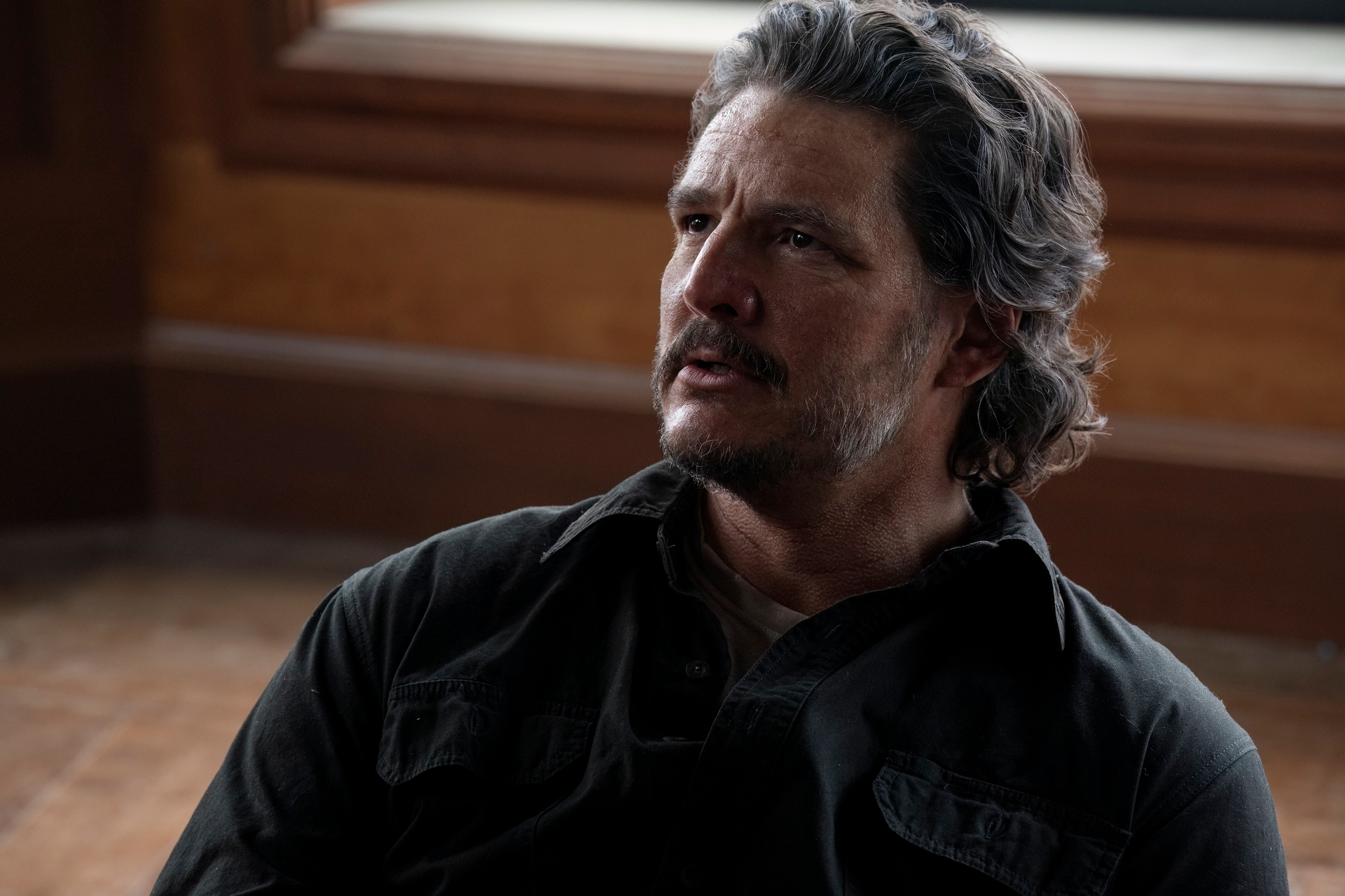 Persona sentada con expresión seria, vistiendo camisa de estilo casual en un entorno interior con luz tenue